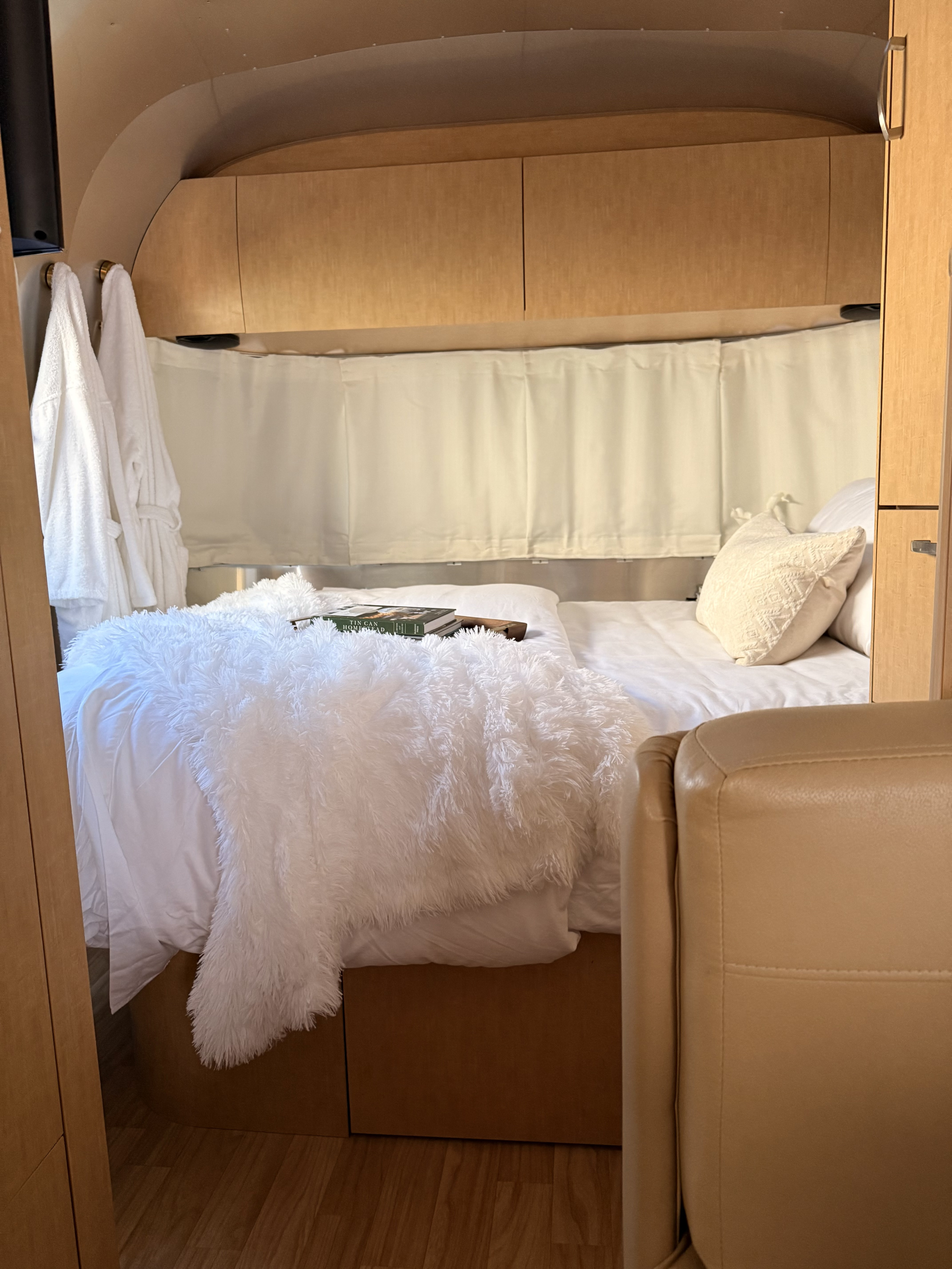 Relax in this cozy rv rental bedroom, featuring white bedding, plush throws, and wood accents.. Airstream Flying Cloud 2017