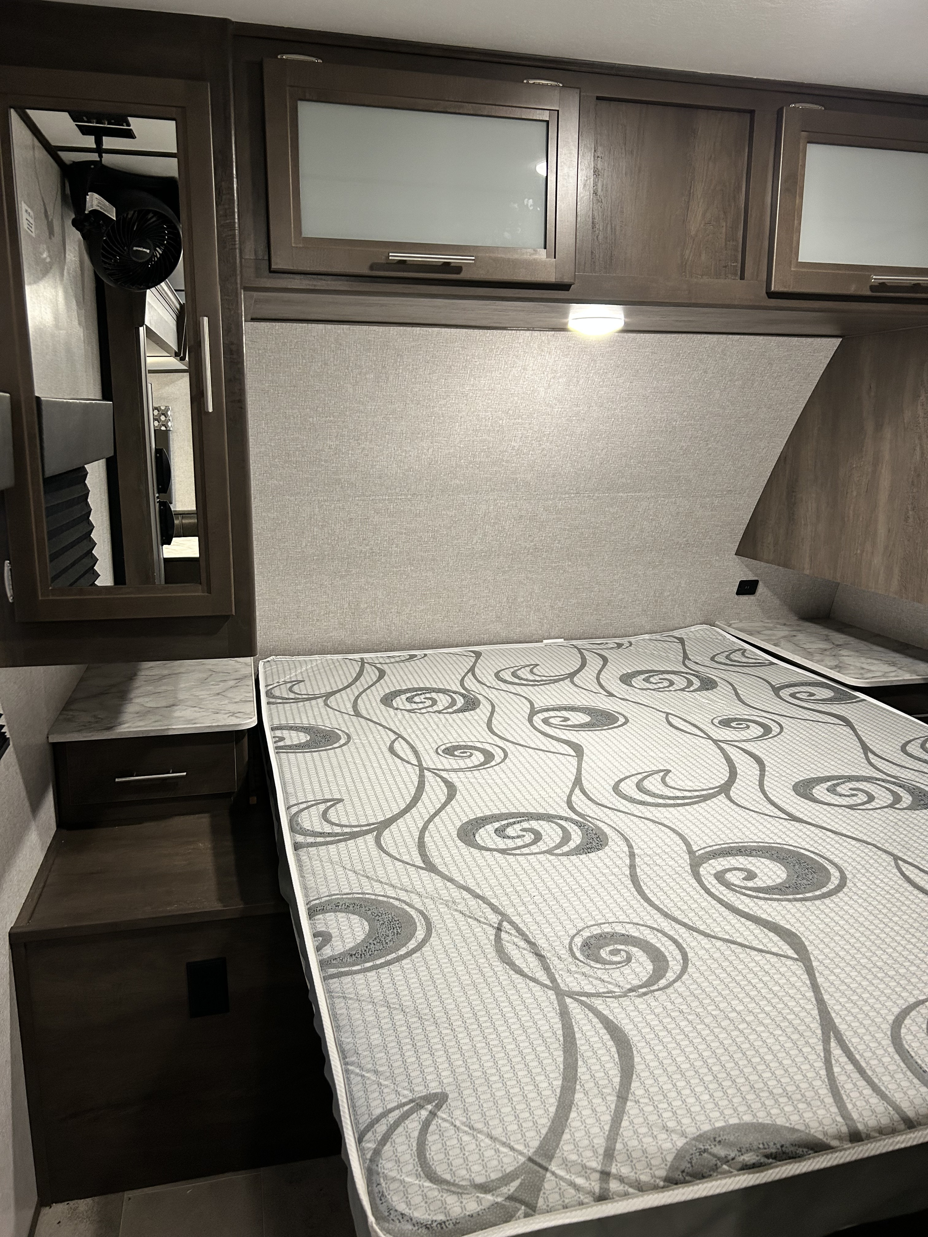 RV rental bedroom featuring a patterned queen mattress, overhead cabinets, and bedside storage.. Dutchmen CM2455BH20 2020