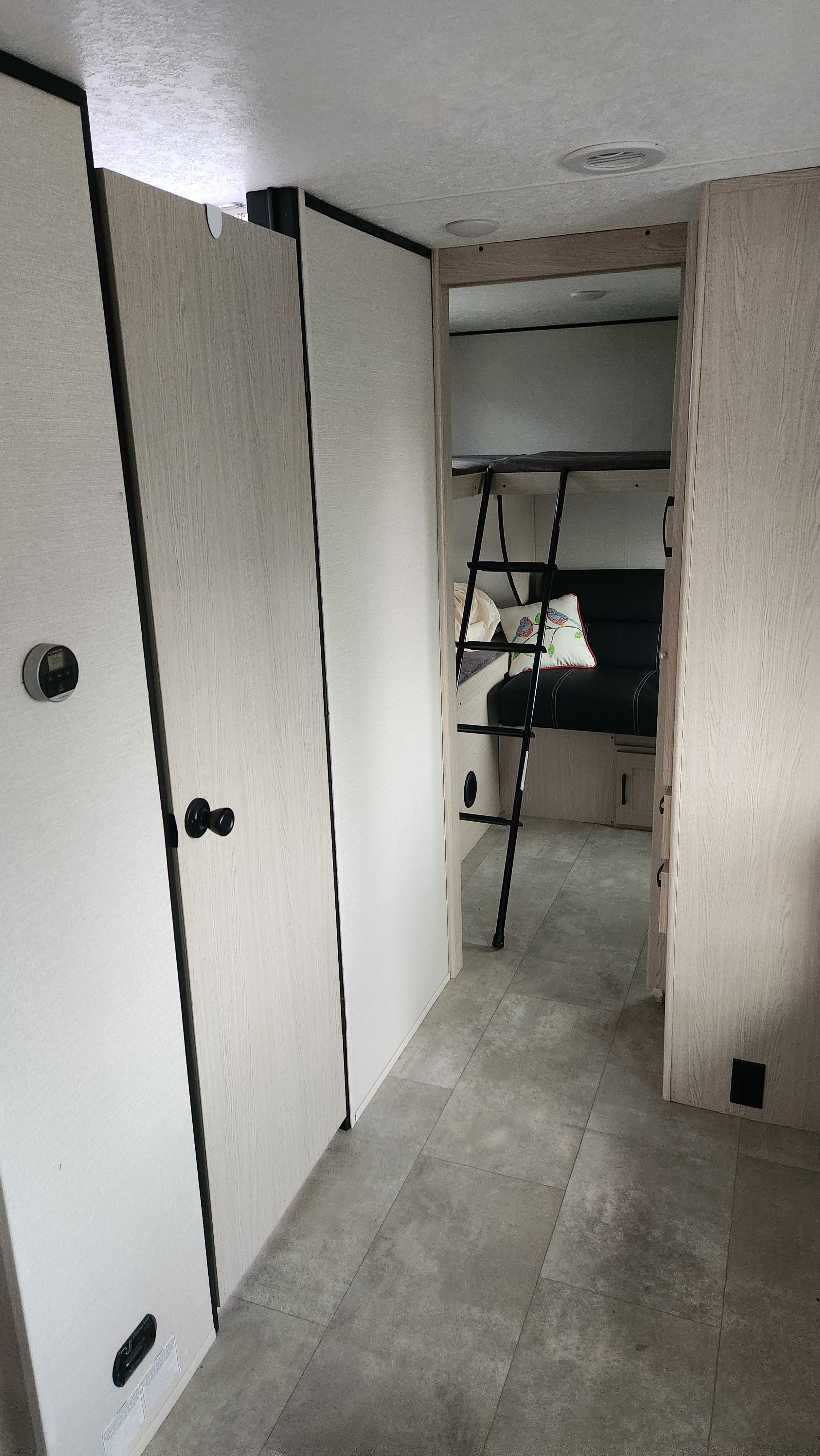 Bright RV rental interior, showcasing a hallway with control panel, storage, and bunk beds with a ladder & sofa.. Coachmen Apex 2021