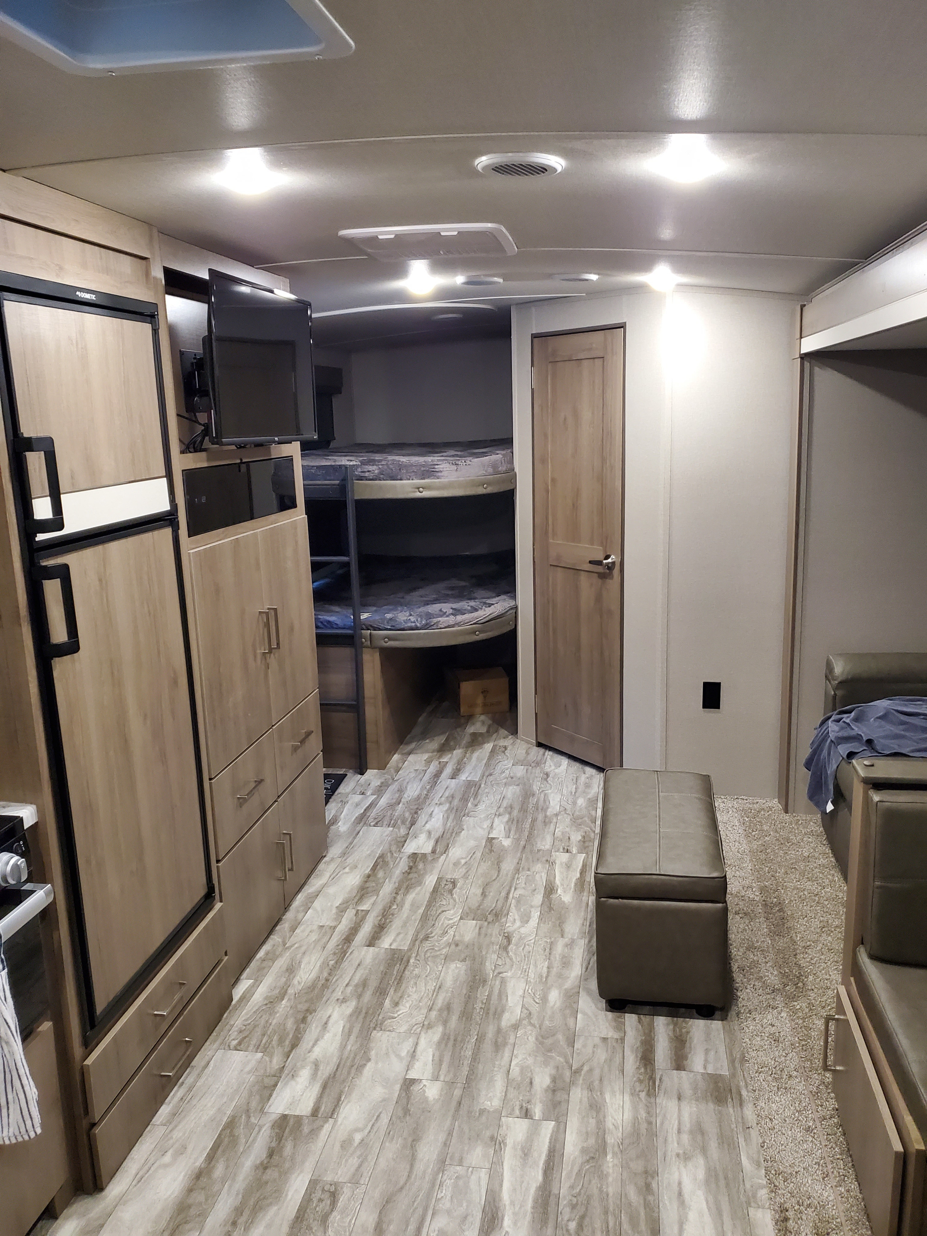 RV rental interior: kitchen, fridge, bunk beds, and seating. A practical camper living space with wood-look flooring.. Grand Design Imagine 2022