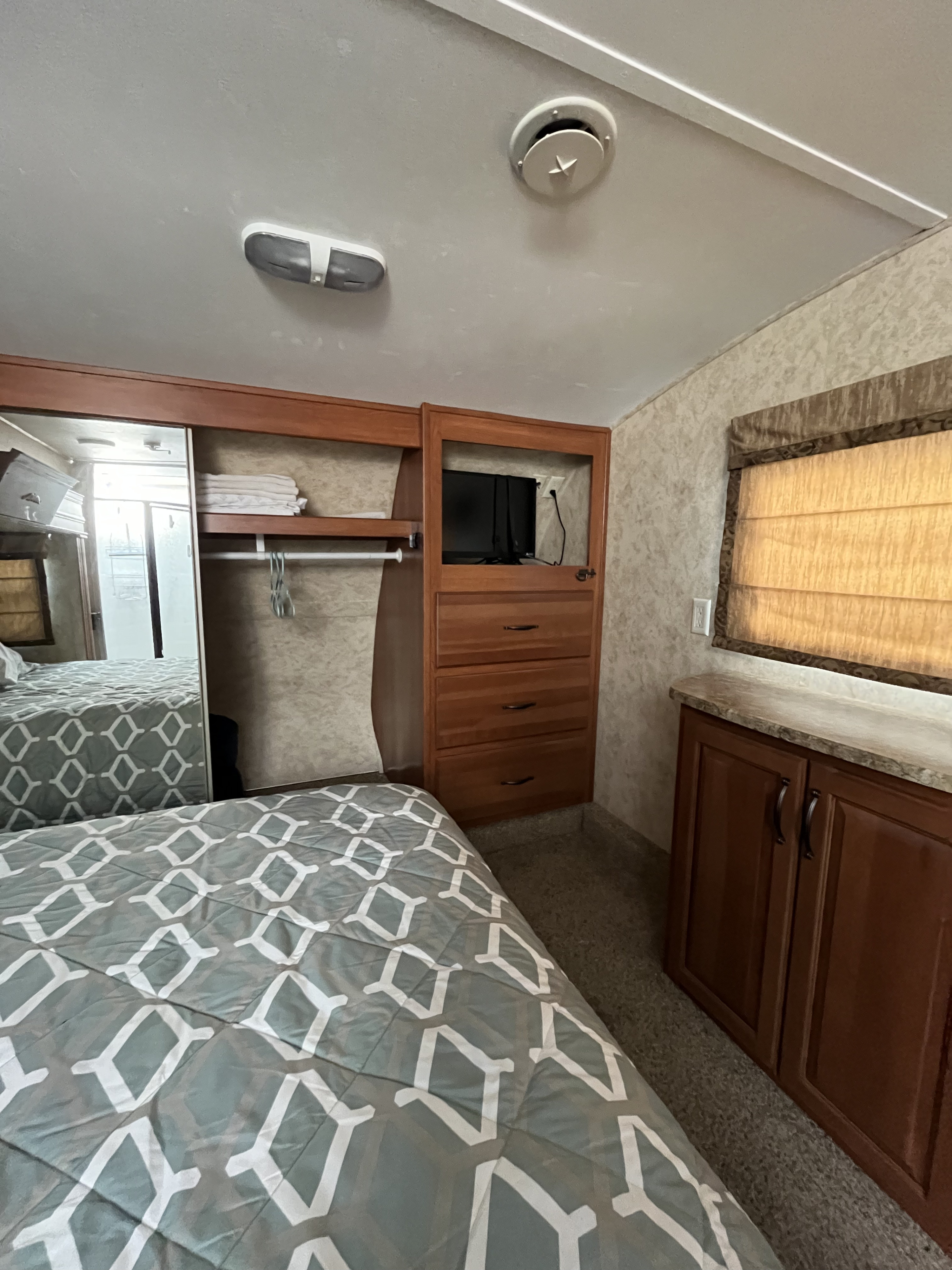 RV rental bedroom interior with a diamond patterned bedspread, mirrored wardrobe, and built-in dresser with TV.. Keystone RV Cougar 2011