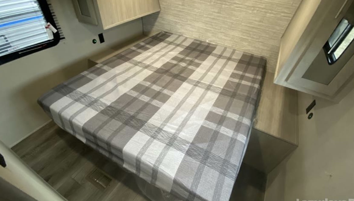 Cozy RV rental bedroom with a plaid bed, overhead cabinets, and a window.. Forest River Catalina 2022
