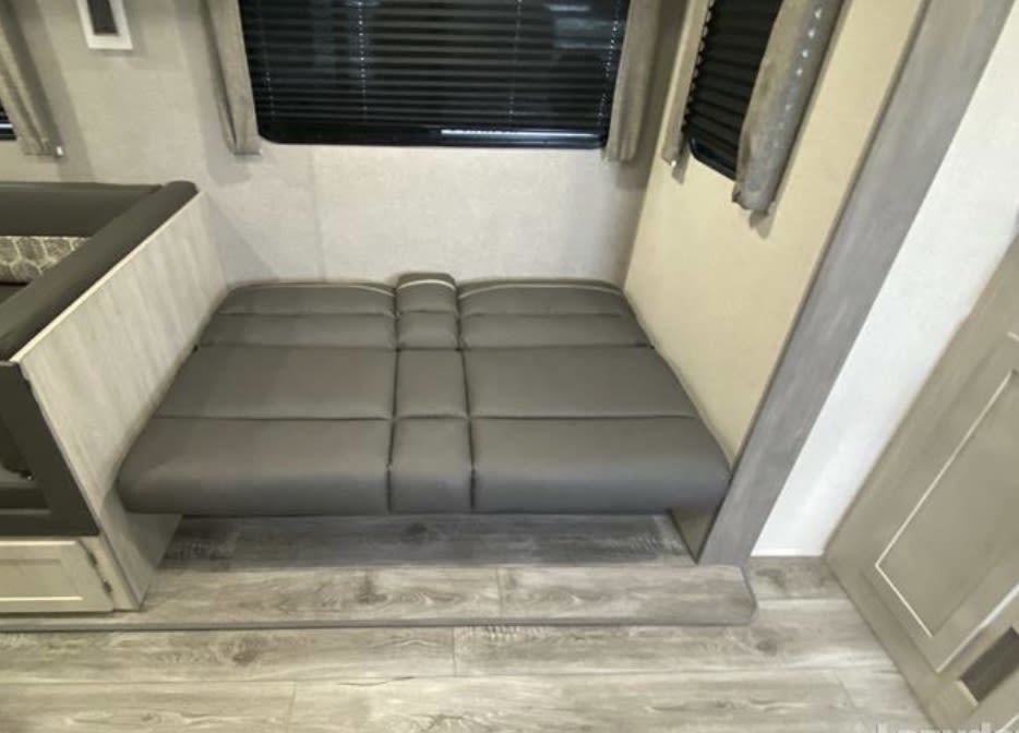 RV rental interior: A gray padded dinette seating, convertible to a bed, with windows and blinds visible. Cozy sleeping space.. Forest River Catalina 2022