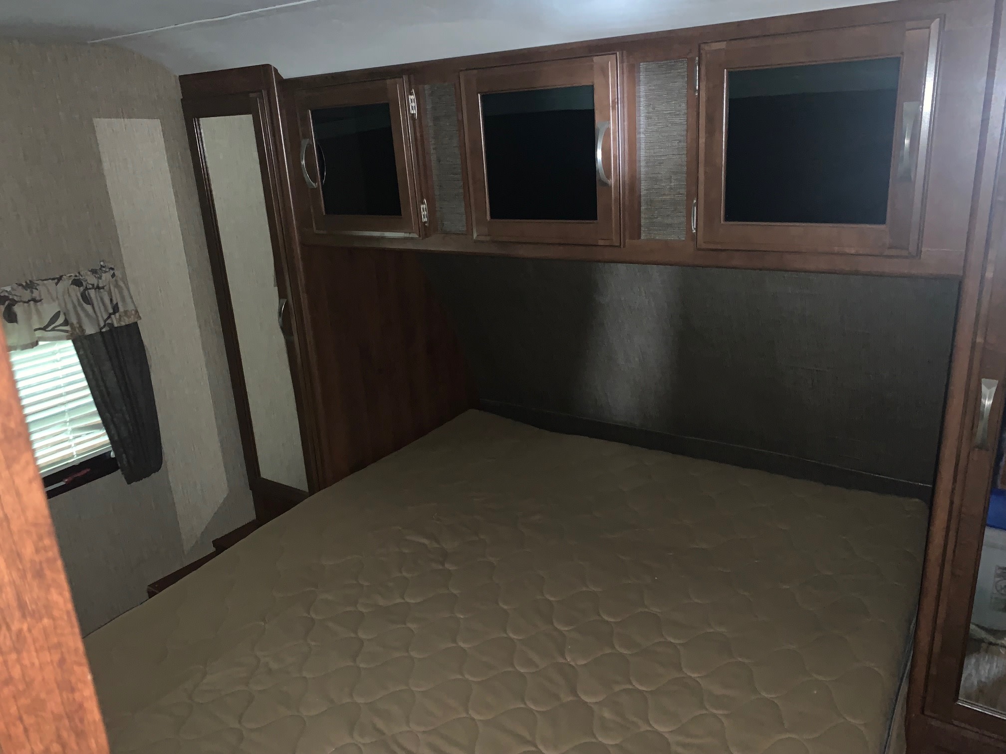 Cozy RV rental bedroom featuring a mattress, overhead storage cabinets, and a window with blinds.. Keystone RV Passport Grand Touring 2016