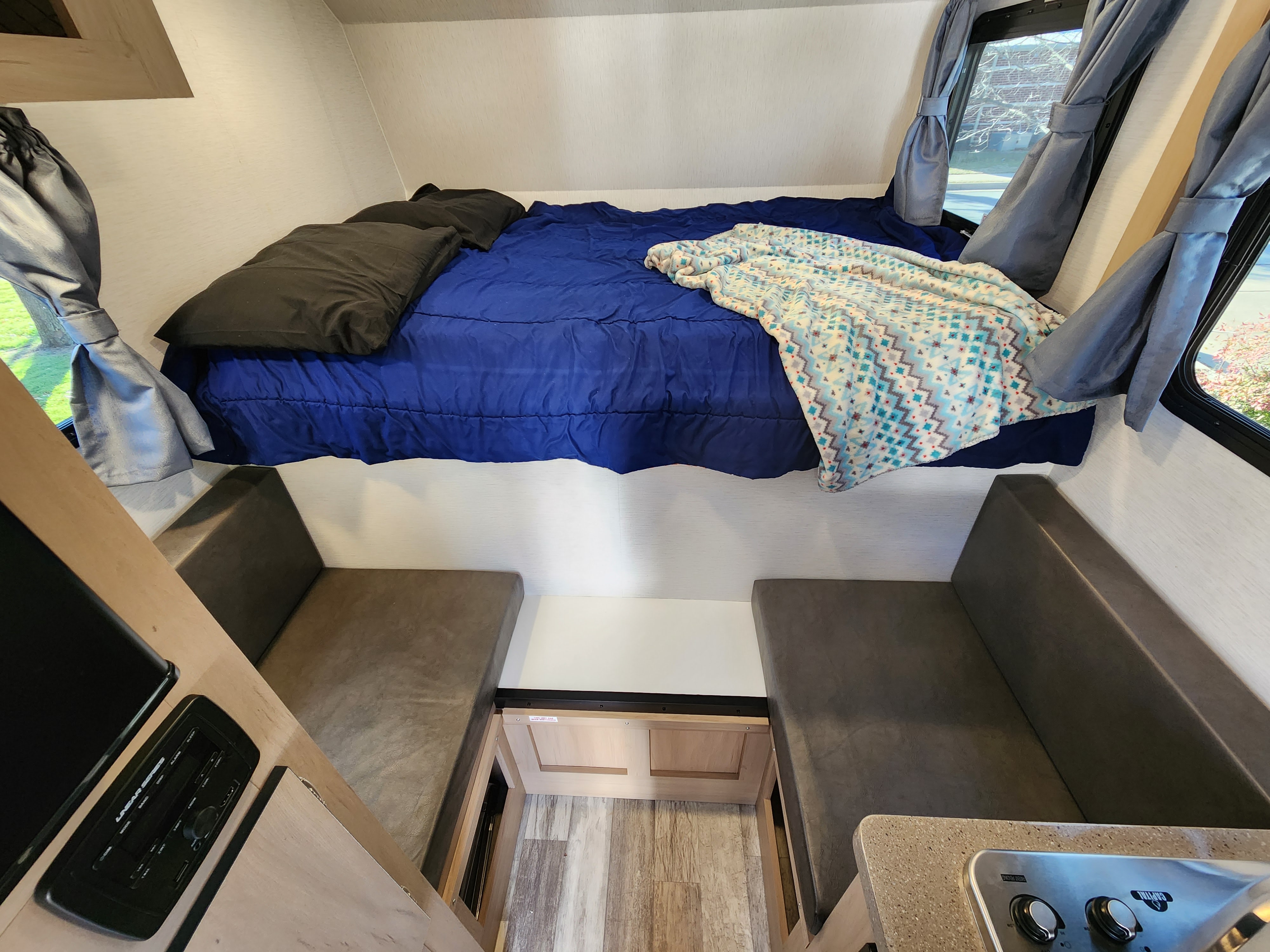 Cozy RV rental interior: elevated bed, dinette seating, and compact kitchen area for travel comfort.. Travel Lite Atom 600a 2025