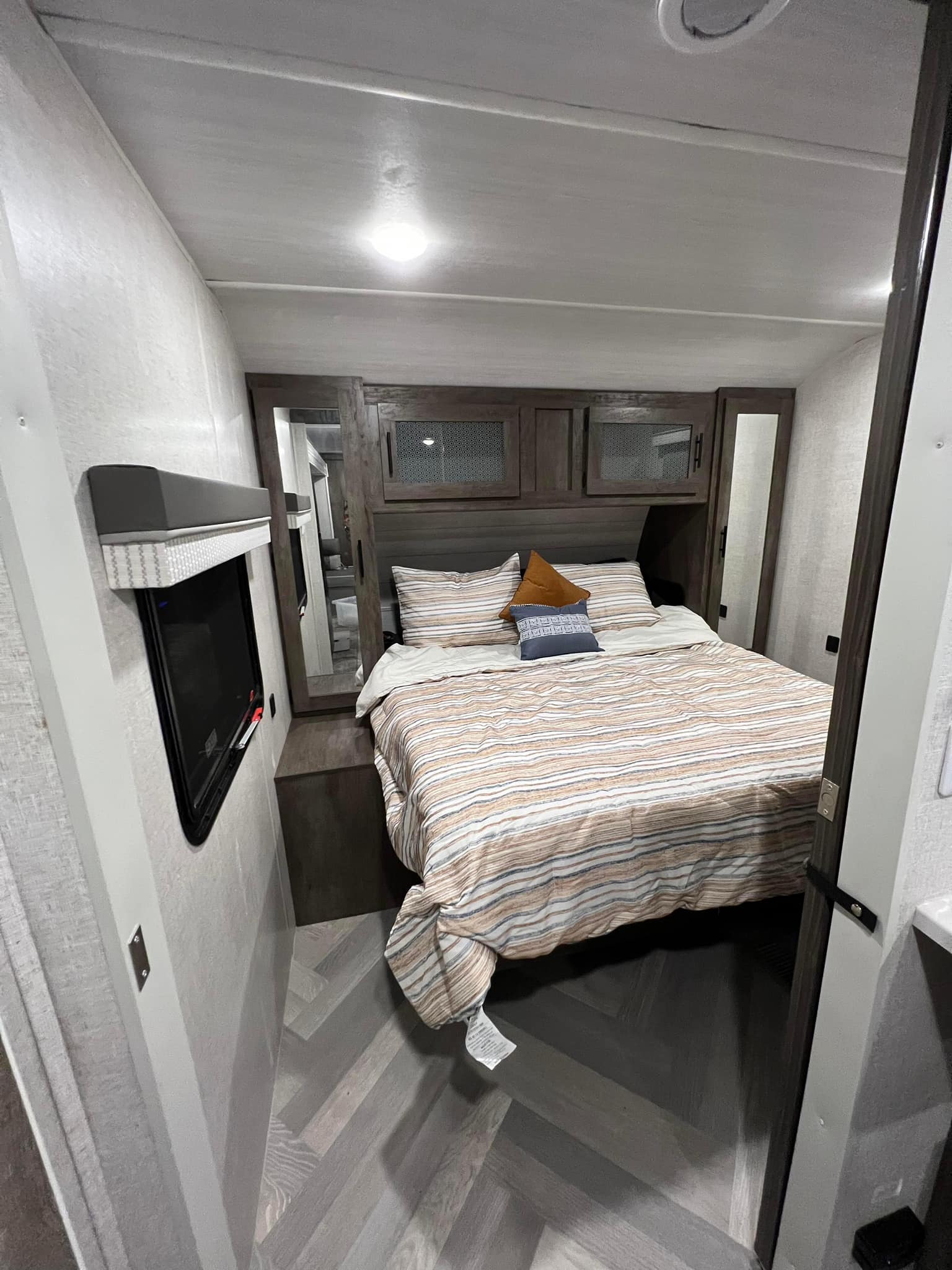 Cozy RV rental bedroom featuring a striped bed, overhead storage, and herringbone flooring. Ideal for comfortable travel.. FOREST RIVER 22RBS 2021