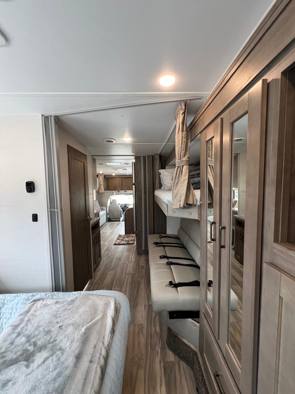 Spacious RV rental interior featuring a bunk bed, sofa with seatbelts, and clear hallway to the front cab. Ideal for family travel.. Gulf Stream Conquest 2025