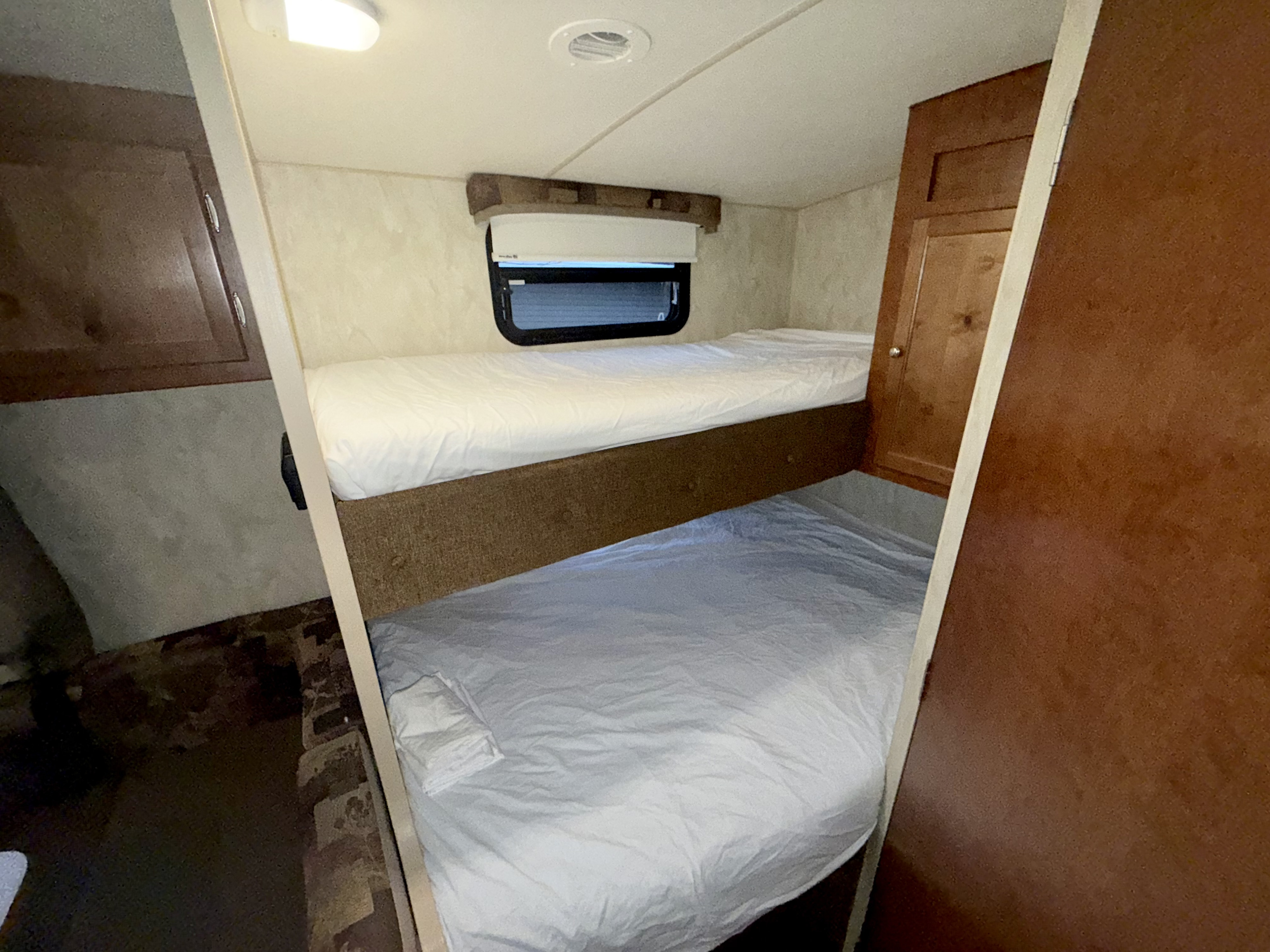 Interior of an RV rental showing two neatly made bunk beds, a side window, and built-in storage.. Nash Nash Trailer 2016