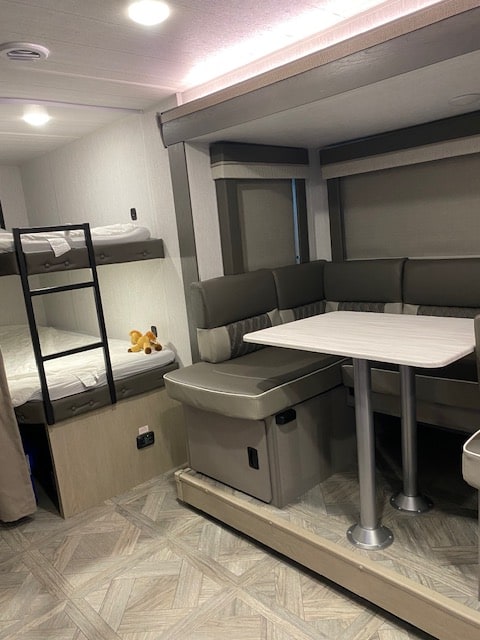 Modern RV rental interior showing bunk beds with ladder on left, and a comfortable U-shaped dinette with table on the right.. FOREST RIVER 263BHLX 2024