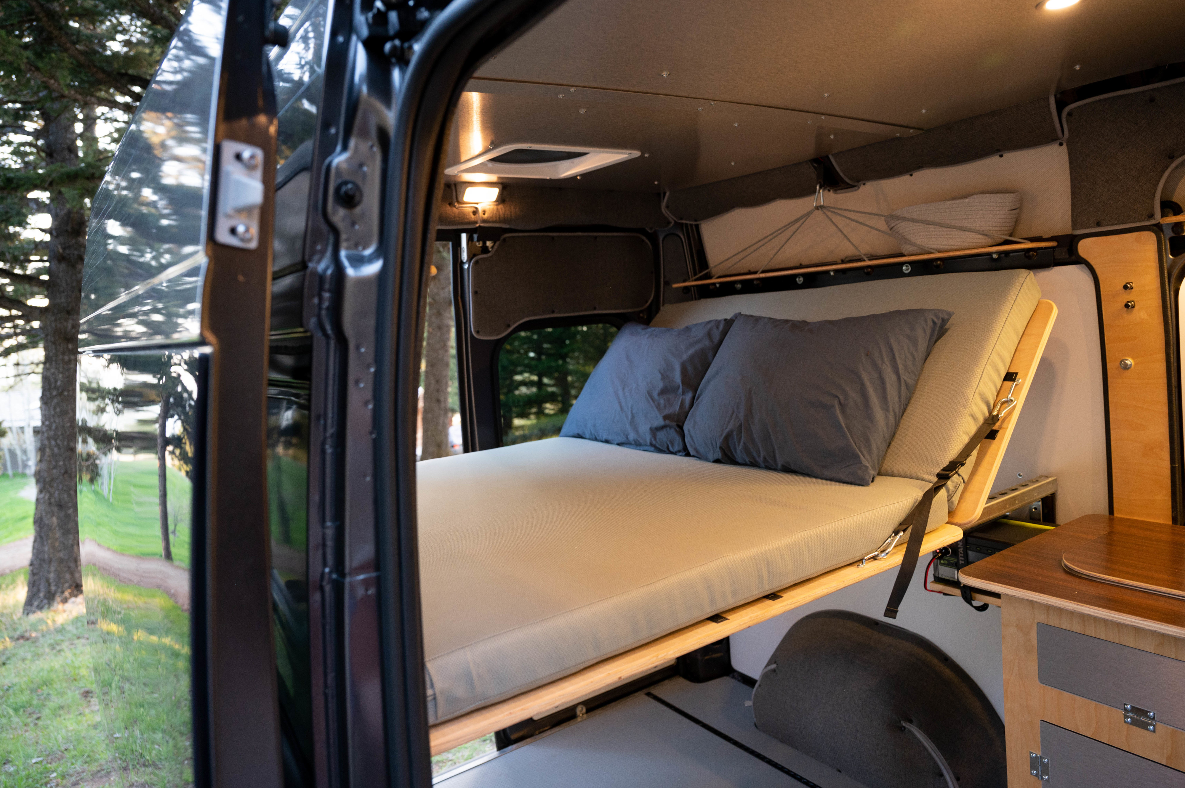 Explore this cozy RV rental campervan interior. A comfortable bed, storage, and scenic outdoor views from the open side door.. Dodge Promaster 2021