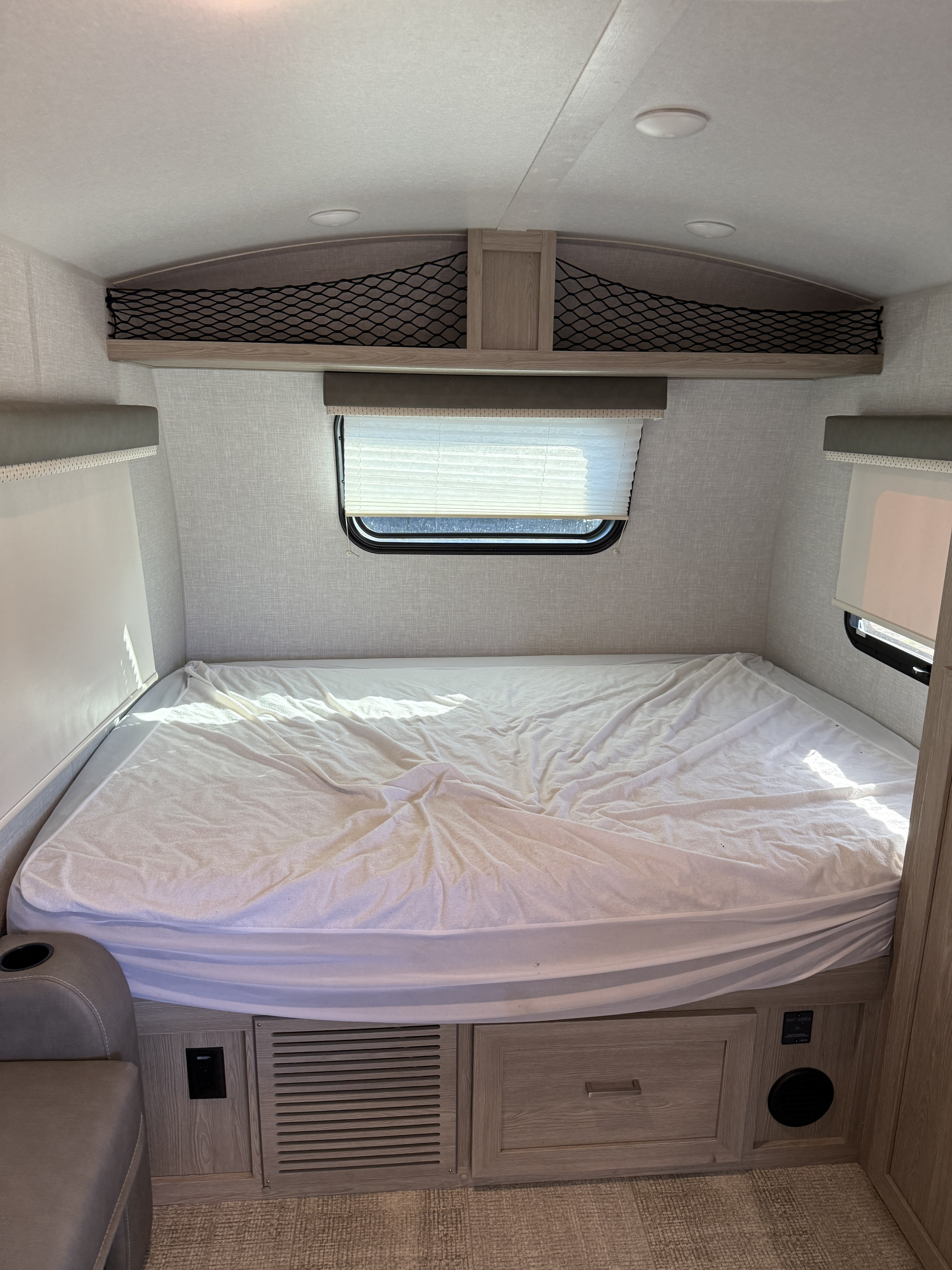 A compact RV rental bedroom featuring a bed, window with blinds, overhead storage netting, and built-in amenities.. Forks Rv Rockwood Geo Pro 2021