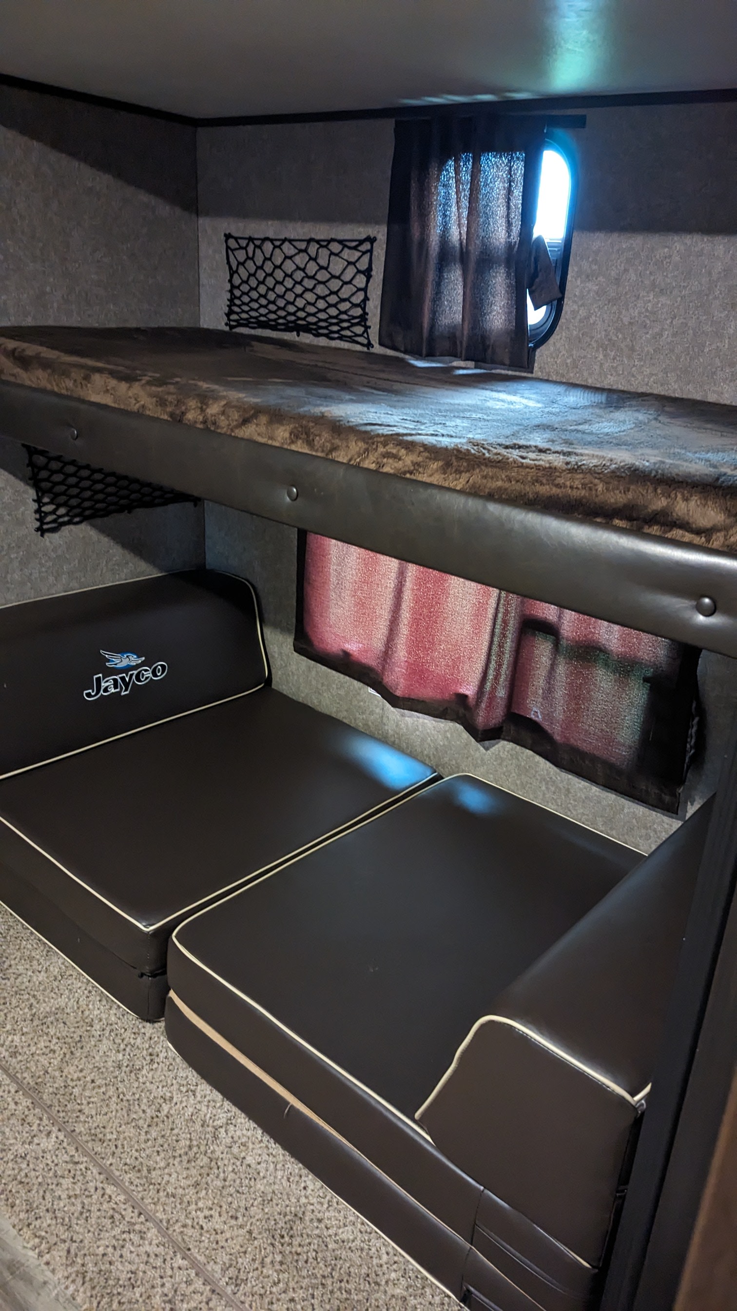 RV rental with black bunk beds & seating area. Features storage nets and a small window for a compact sleeping space.. Jayco Jay Flight 2019