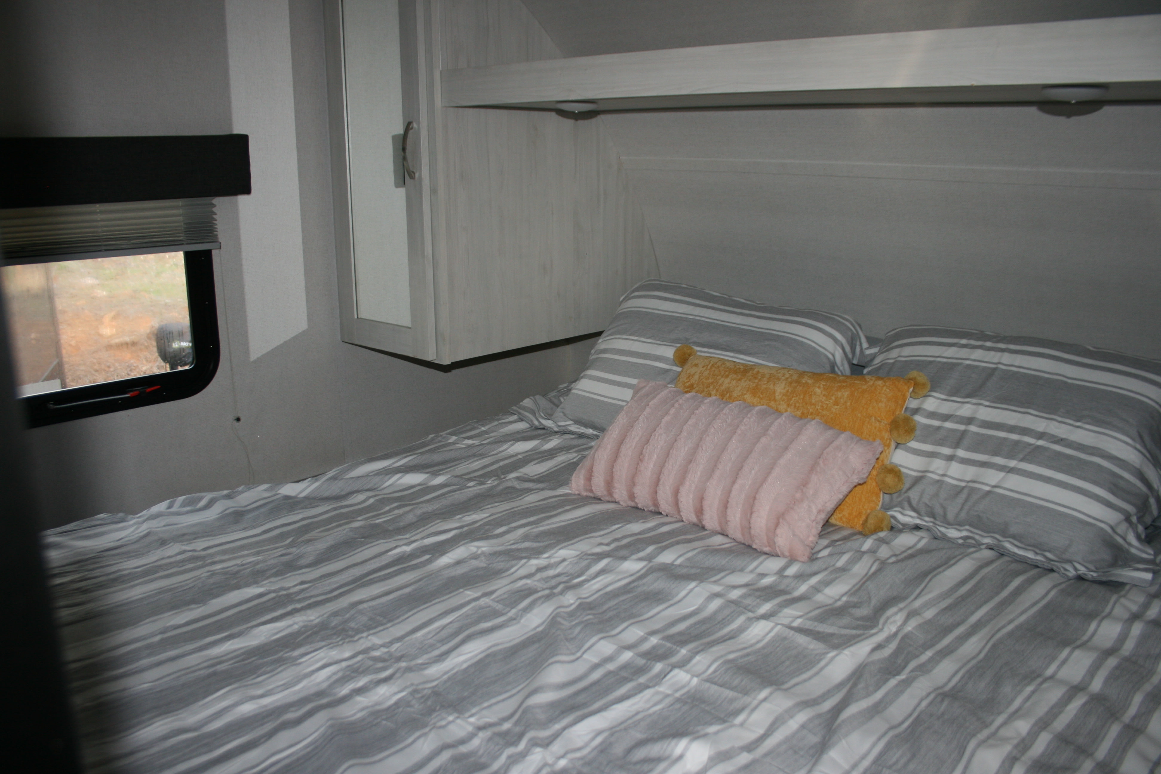 Relaxing RV rental bedroom: striped bed, cozy pillows, window with blinds, and overhead cabinet storage for your travels.. Forest River Tracer 2022