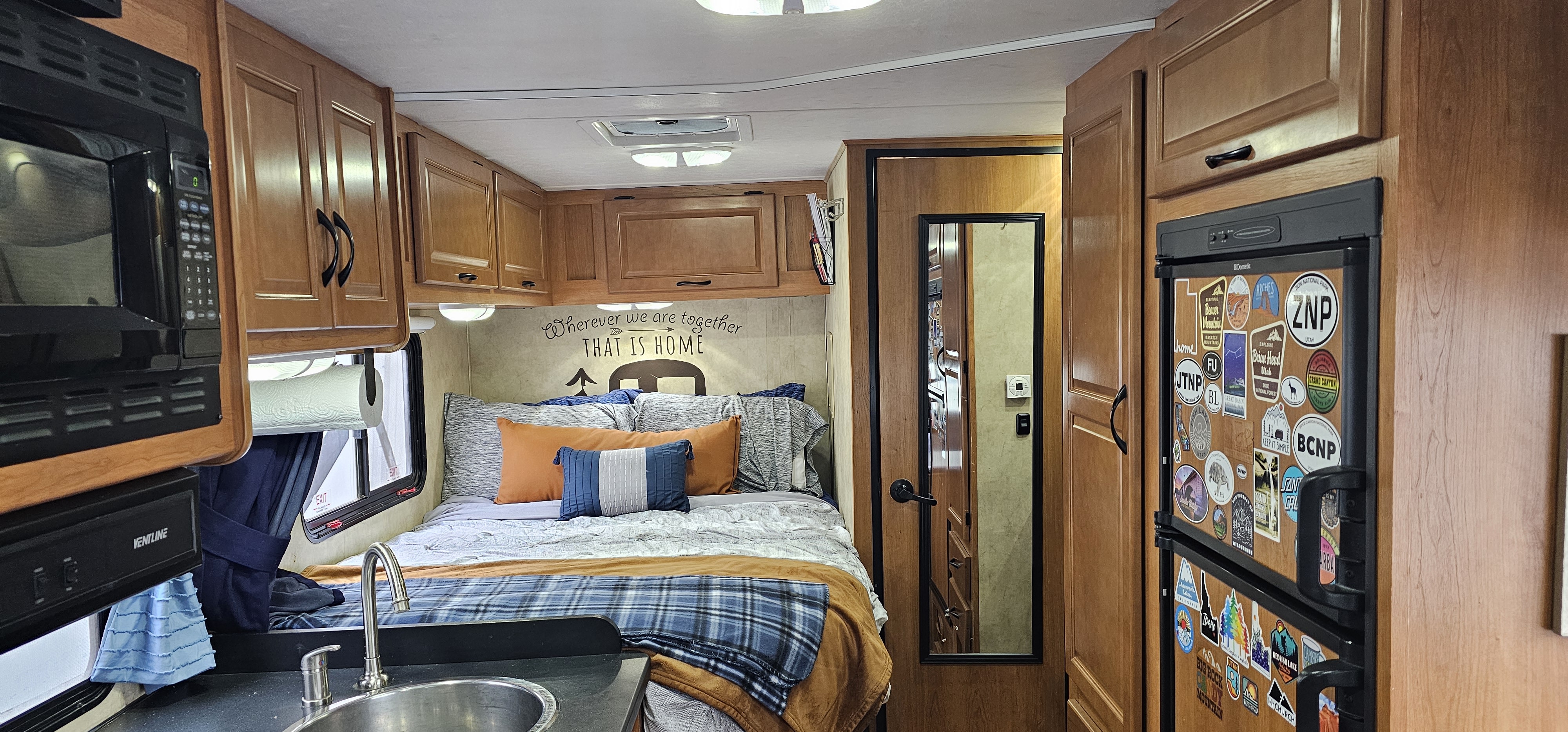 Cozy RV rental interior with a bed, compact kitchen, and refrigerator adorned with national park stickers, perfect for travel.. Thor Majestic 2014