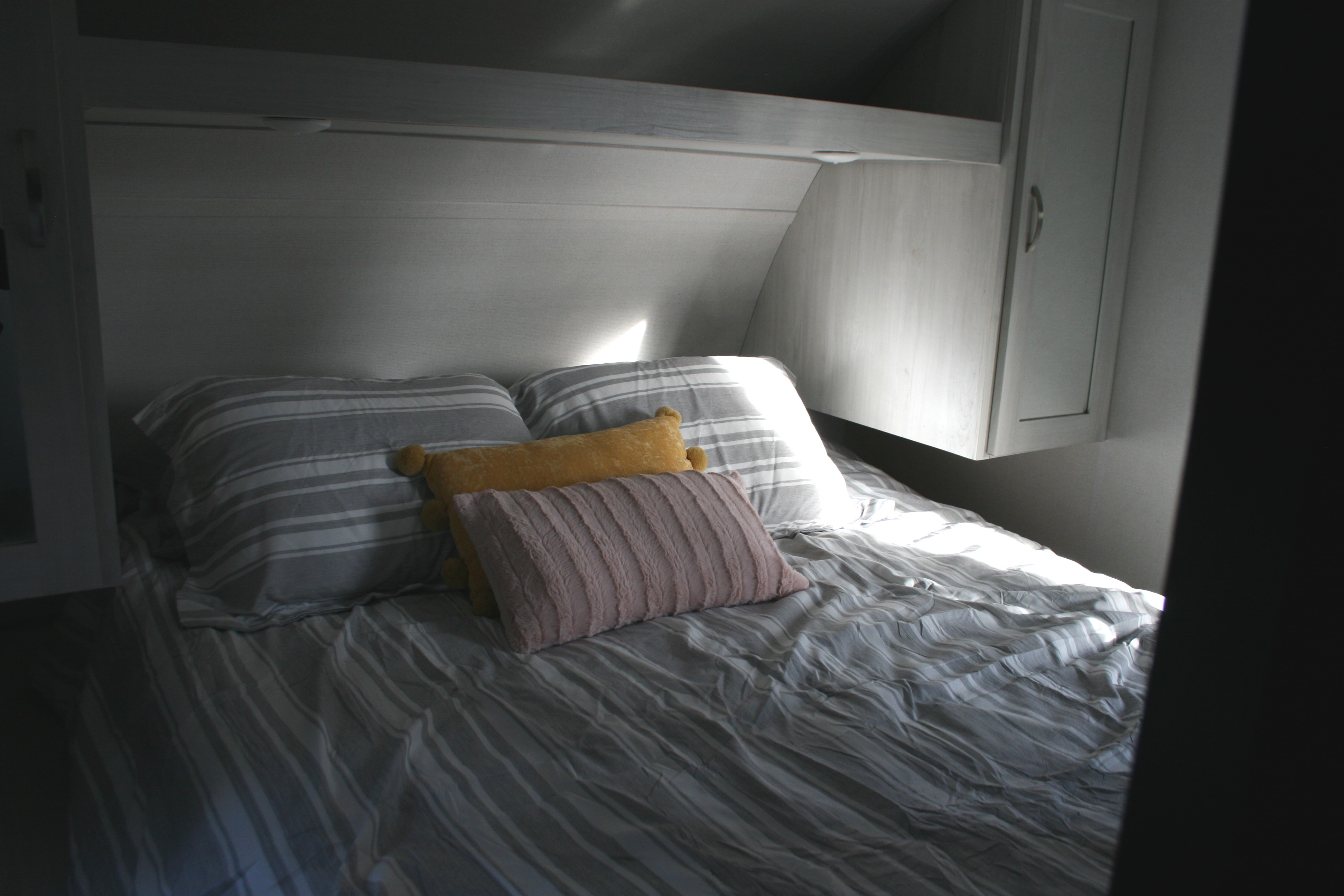Bright RV rental bedroom: striped bed, two large, one yellow, and one pink pillow. Light wood interior.. Forest River Tracer 2022