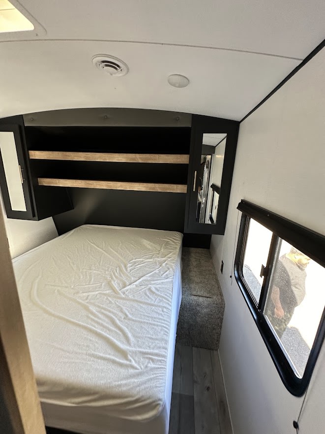 Spacious RV rental bedroom with queen bed, ample overhead storage, and a large window, perfect for your next adventure.. Keystone Springdale 2023