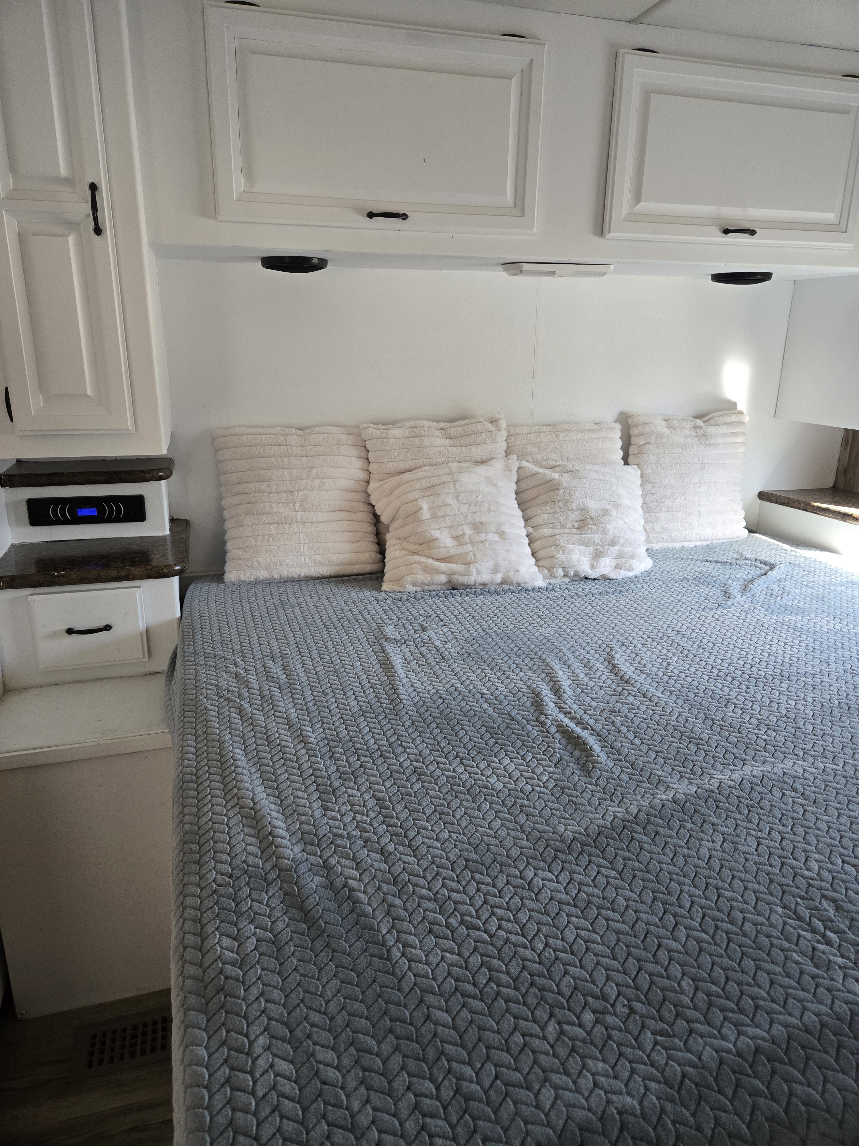 Cozy RV rental bedroom with white storage cabinets, soft white pillows, and a grey patterned blanket. Electronic panel visible.. Thor Motor Coach Hurricane 2015