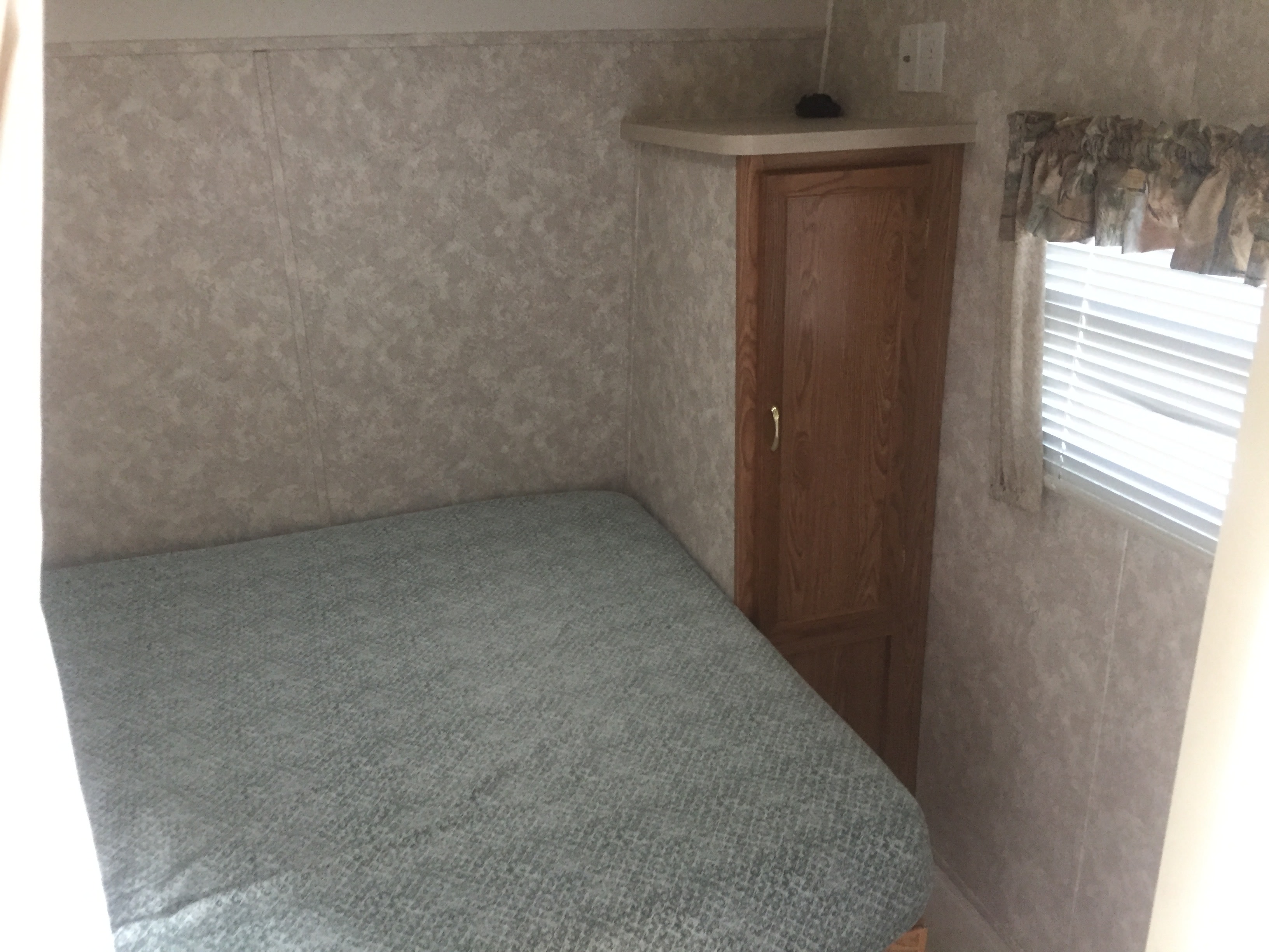 RV rental interior: a compact bedroom with a bed, wooden cabinet, and window with blinds.. Coachmen Bunks 2003