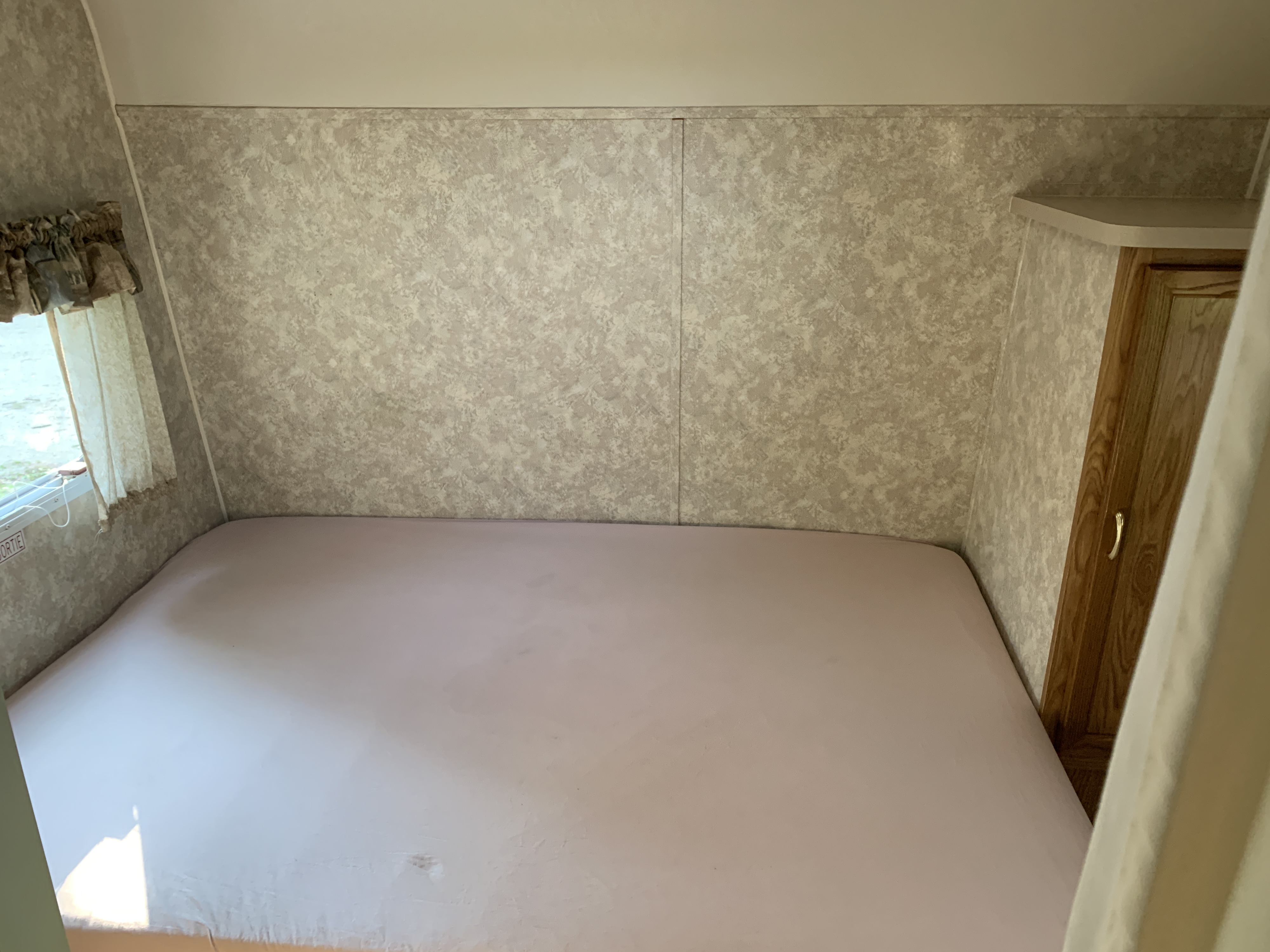 Spacious, clean RV rental bed area with light sheets, patterned walls, and a window.. Coachmen Bunks 2003