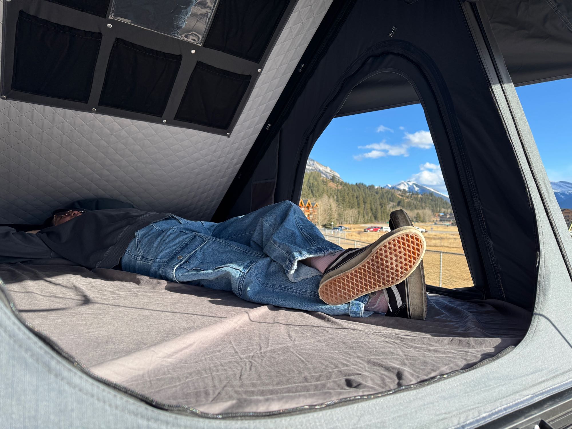 Inside an RV rental, a person relaxes on a comfy bed, looking out at snow-capped mountains and a forest.. Dodge Caravan 2016