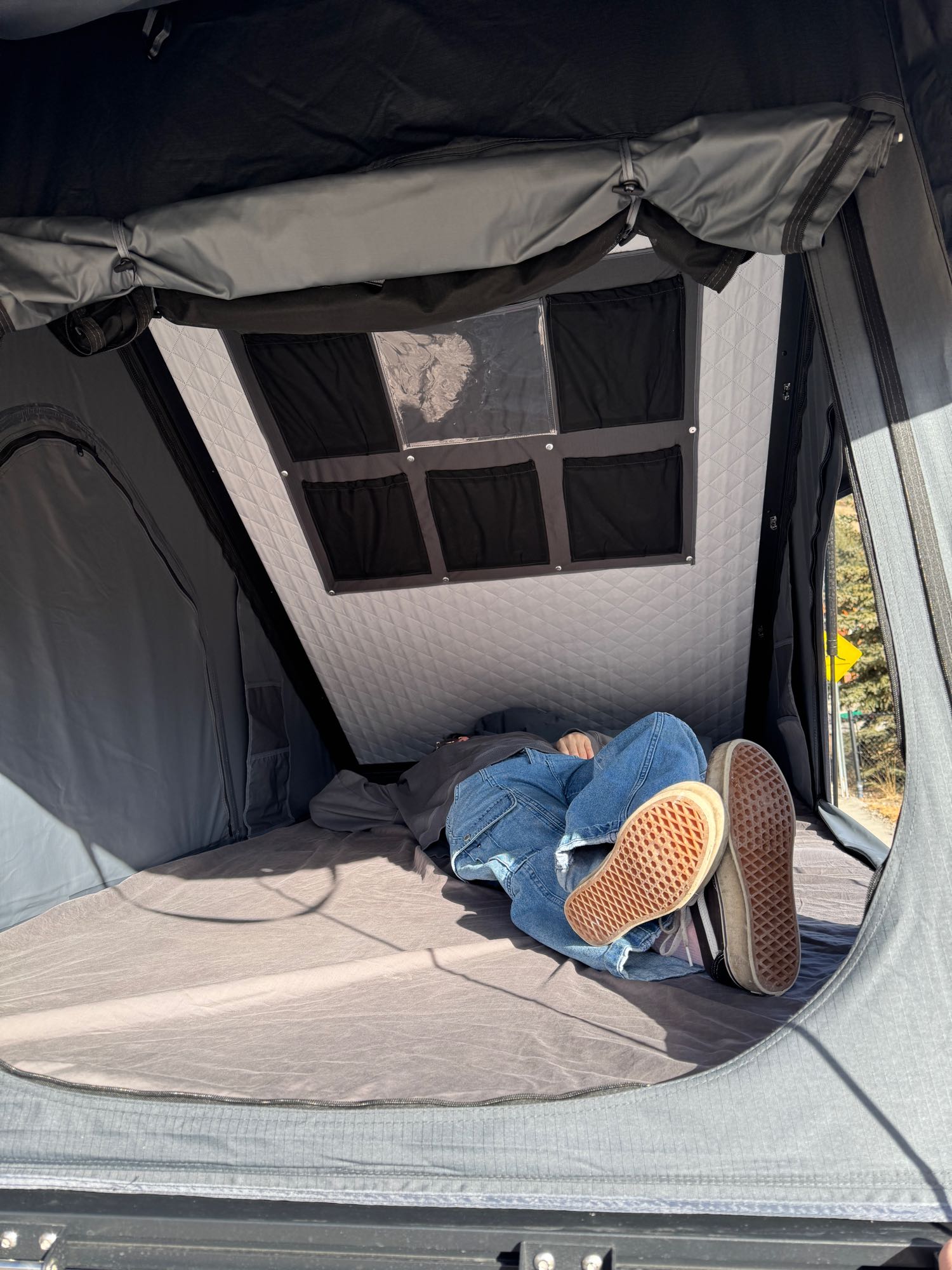 Relaxing inside an RV rental's rooftop tent, a person naps comfortably, perfect for travel & outdoor leisure.. Dodge Caravan 2016