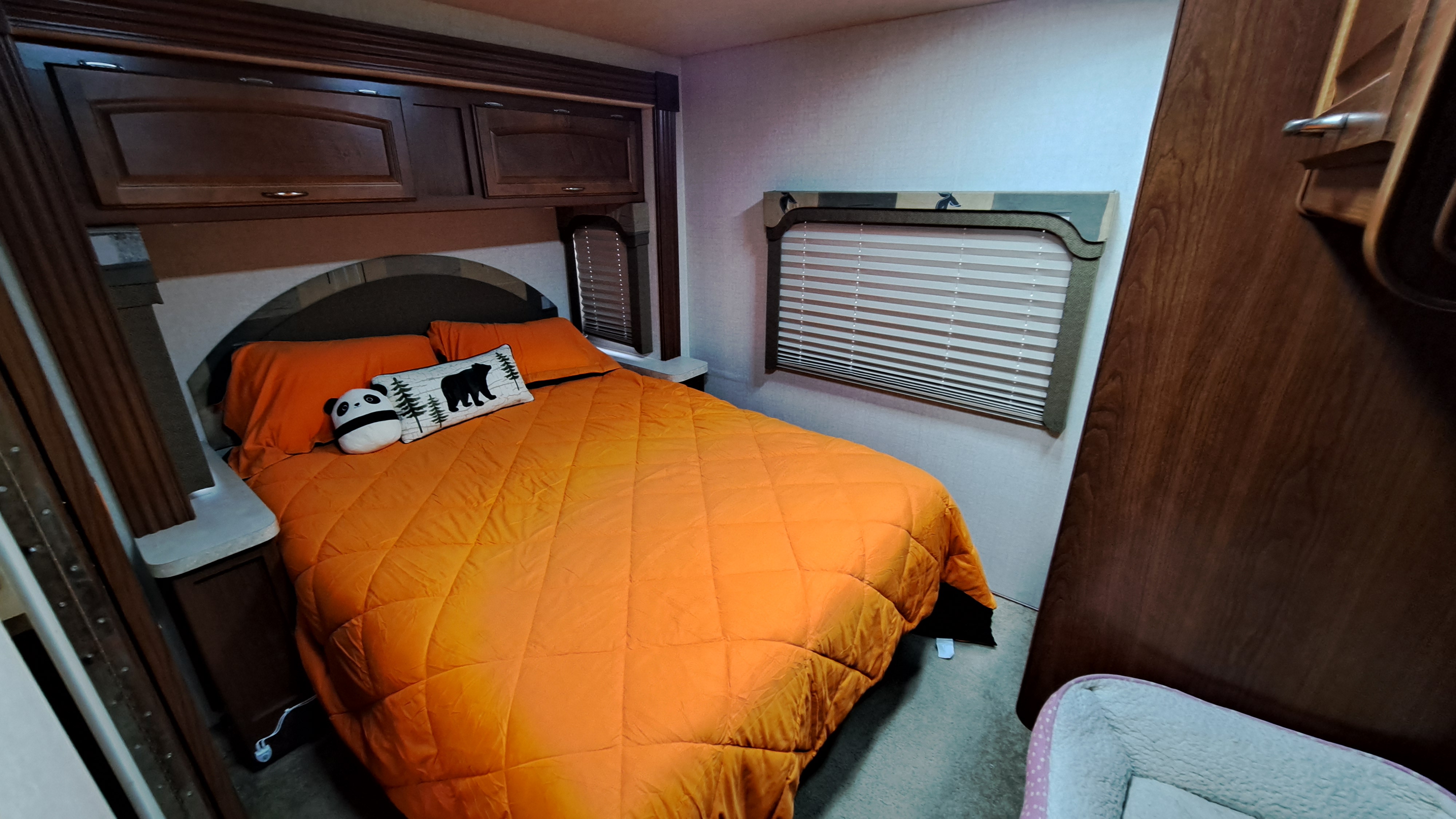 Cozy RV rental bedroom featuring an orange bed, panda pillow, overhead cabinets, and a window.. Tioga 31M 2008