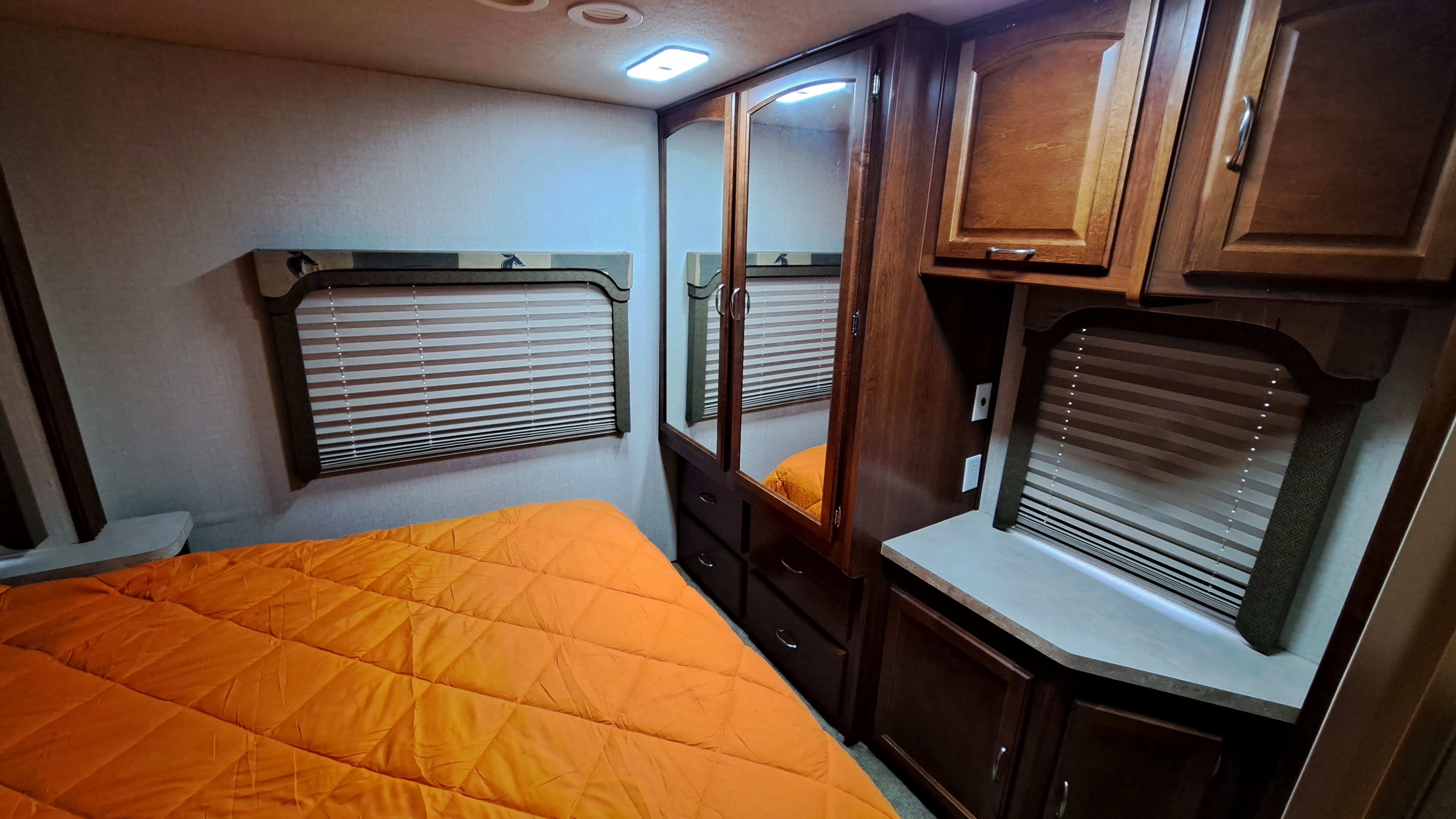 A cozy RV rental bedroom features an orange comforter, wood cabinetry, and window blinds.. Tioga 31M 2008