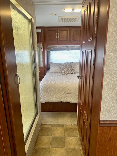 RV rental interior: Tiled hallway leads to a carpeted bedroom with a bed, cabinets, and window. Shower stall on left.. Four Winds Four Winds Motorhome 2006