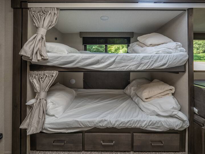 An rv rental's cozy bunk beds, complete with white bedding, pull-back privacy curtains, and convenient under-bed storage drawers.. Grand Design Transcend Xplor 2023