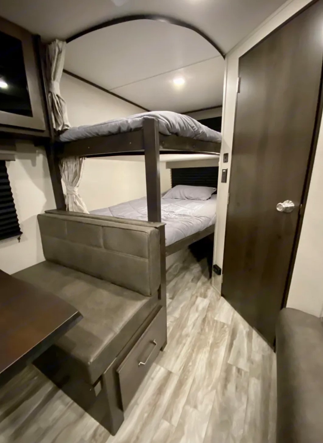 This rv rental features a cozy interior with bunk beds, a dinette table, and wood-look flooring, ideal for compact living.. Grand Design Transcend Xplor 2022