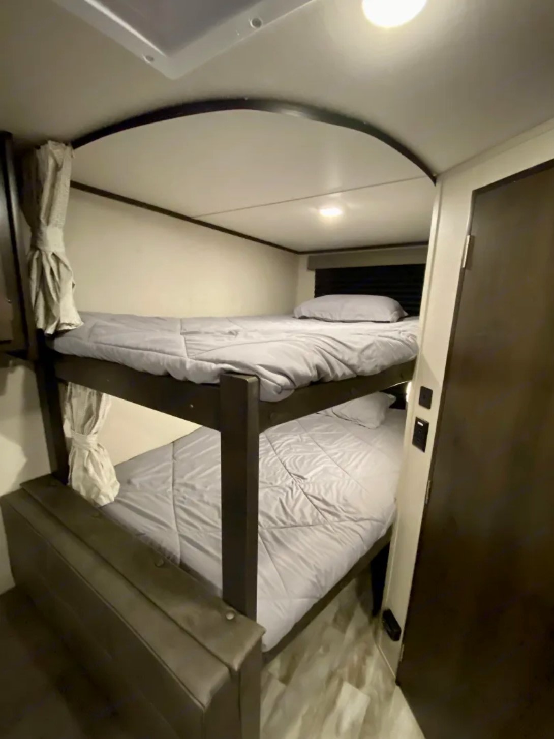 Cozy RV rental interior featuring comfortable bunk beds with grey bedding, ideal for family sleeping. Privacy curtains are visible.. Grand Design Transcend Xplor 2022