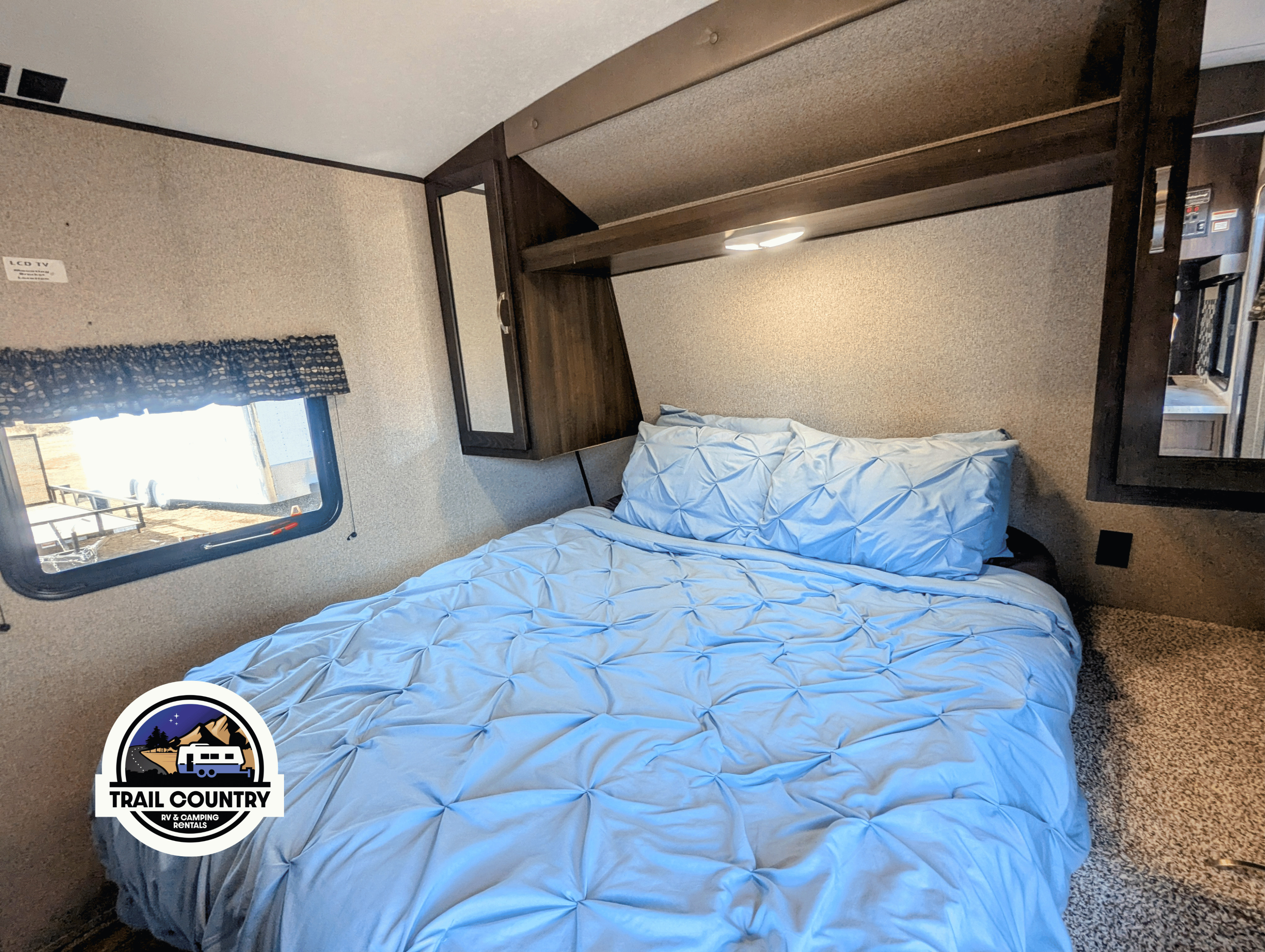 Cozy RV rental bedroom: light blue ruched bed, overhead light, and a window with outdoor view. Ideal for travel.. Keystone RV Springdale 2020