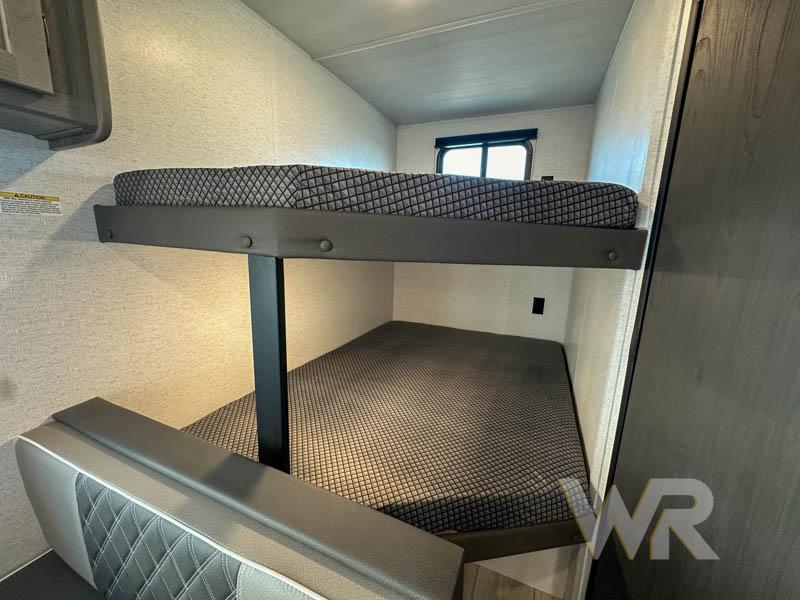 Inside an RV rental, a cozy sleeping area features two bunk beds. The upper bunk has a mattress, and the lower doubles as seating.. Keystone Hideout 240bh 2025