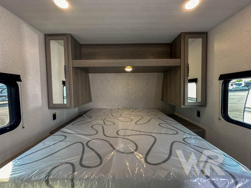 Spacious RV bedroom interior featuring overhead cabinets, side windows, and a comfortable bed. Ideal for your next rv rental.. Keystone Hideout 240bh 2025