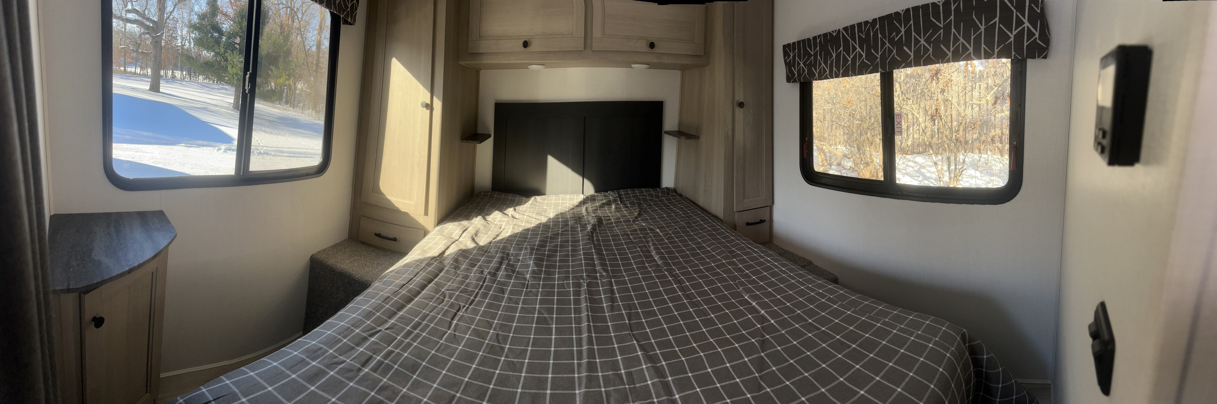 Bright RV rental bedroom features a plaid bed, ample storage cabinets, and scenic snow-covered views from the windows.. Forest River Sunseeker 2025