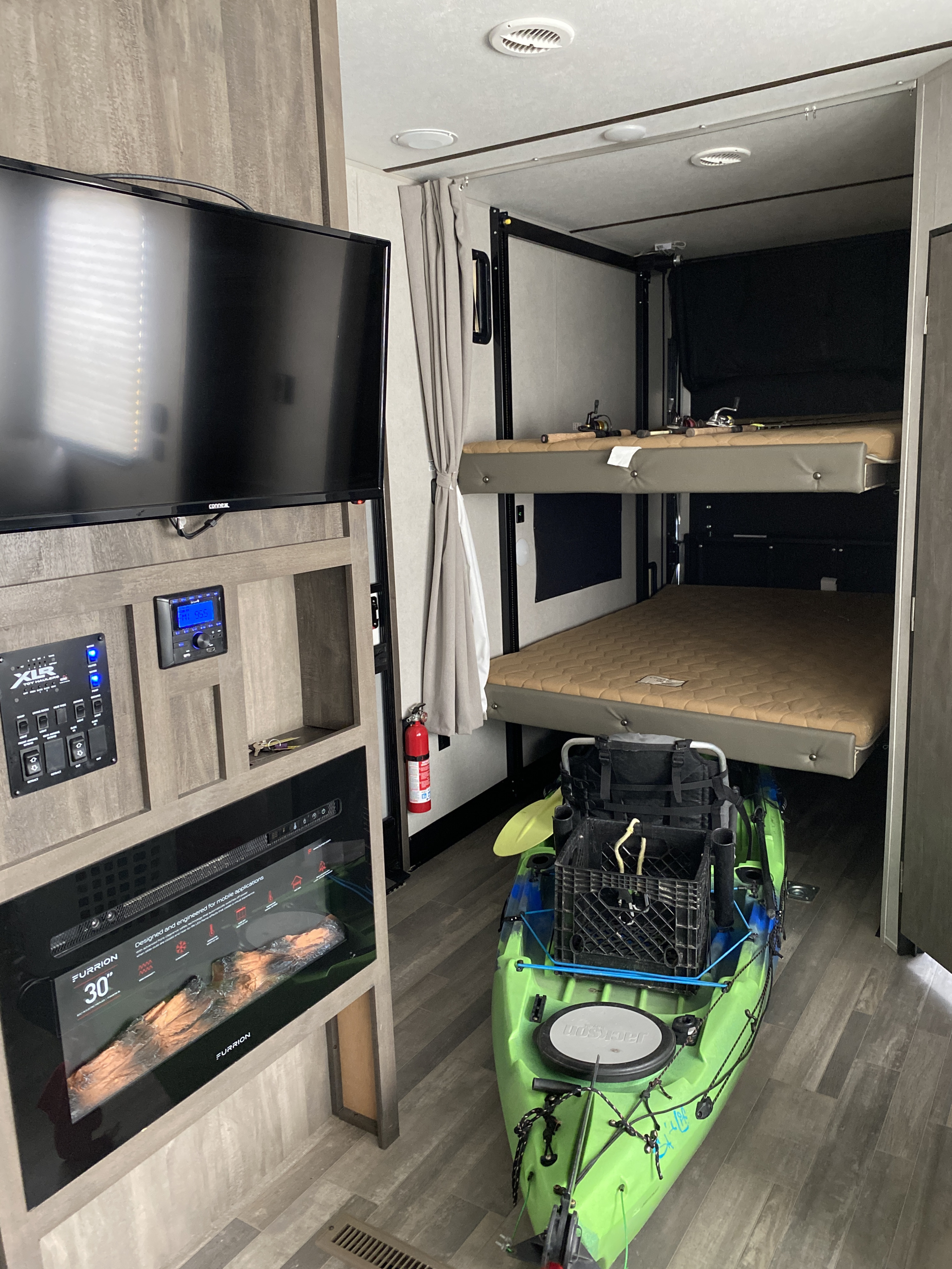 RV rental interior with TV, control panel, fireplace, and bunk beds. A bright green kayak is stored below, ready for adventure.. Forest River Nitro Xlr 2020