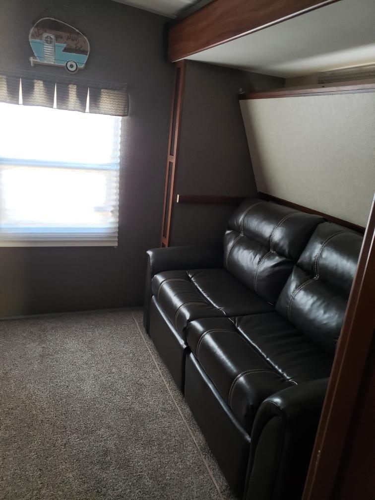 Cozy RV rental interior featuring a dark sofa, bunk above, and bright window. Ready for your travels!. Heartland RVs Mallard 2017