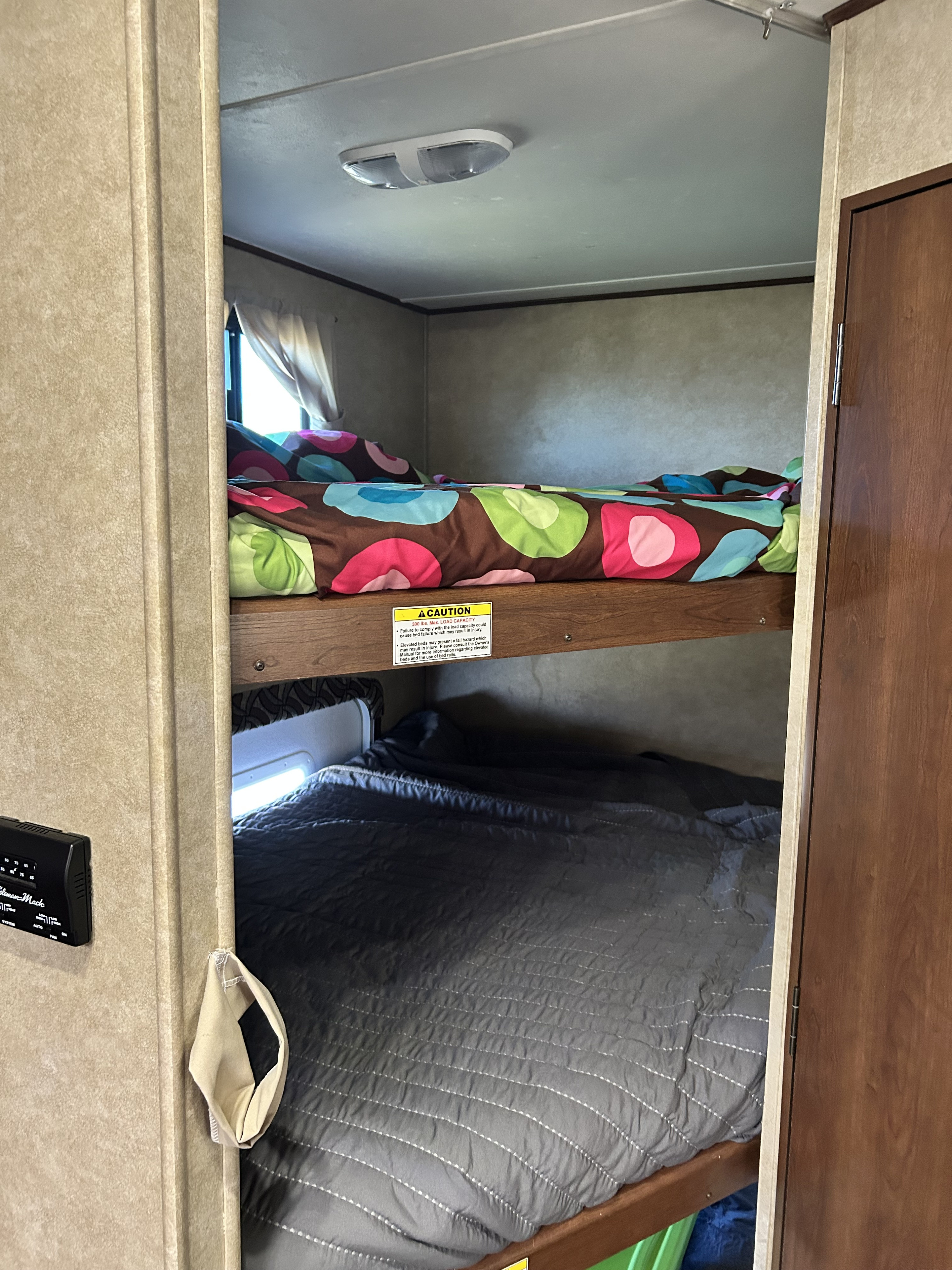 RV rental bunk beds, offering comfortable sleeping in a compact interior. Top bunk has colorful bedding, bottom has dark quilt.. Crossroads RV Zinger 2015