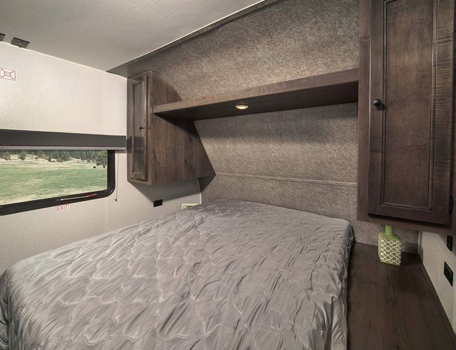 Cozy RV rental bedroom featuring a grey bed, window with nature views, and functional dark wood storage.. Starcraft Autumn Ridge 2022