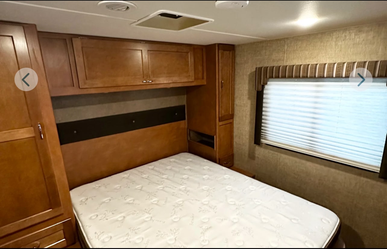 Inside a clean RV rental bedroom: a comfortable bed, wood cabinetry, and window with privacy blinds.. Winnebago Minnie Winnie 2018