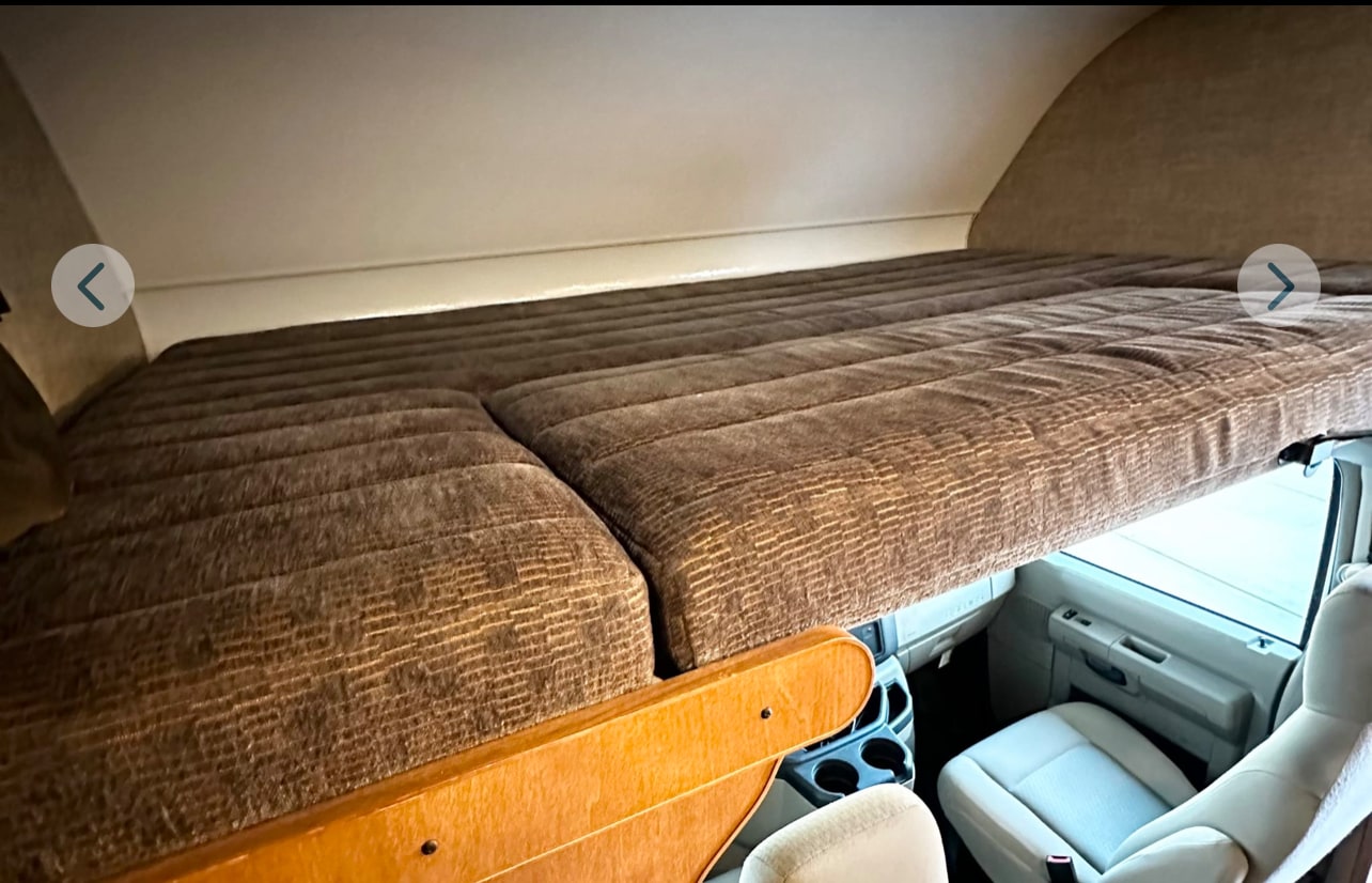 Spacious cab-over bed in an RV rental. Features a large brown quilted mattress overlooking the driver's cabin.. Winnebago Minnie Winnie 2018