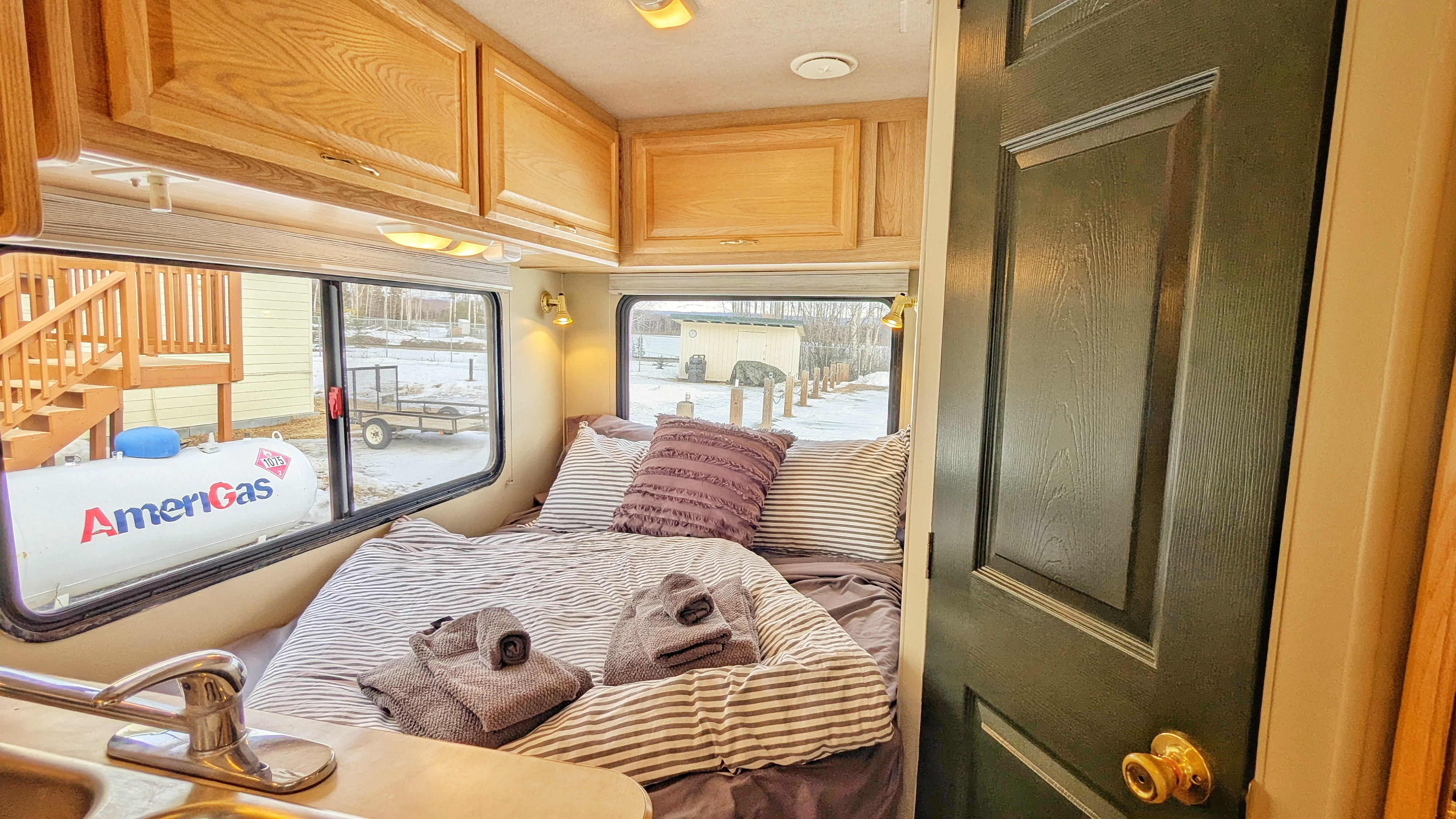 Cozy RV rental interior: a bed with striped linens, wood cabinets, a sink, and a winter view of an AmeriGas tank.. Tioga Tioga Motorhome 2004