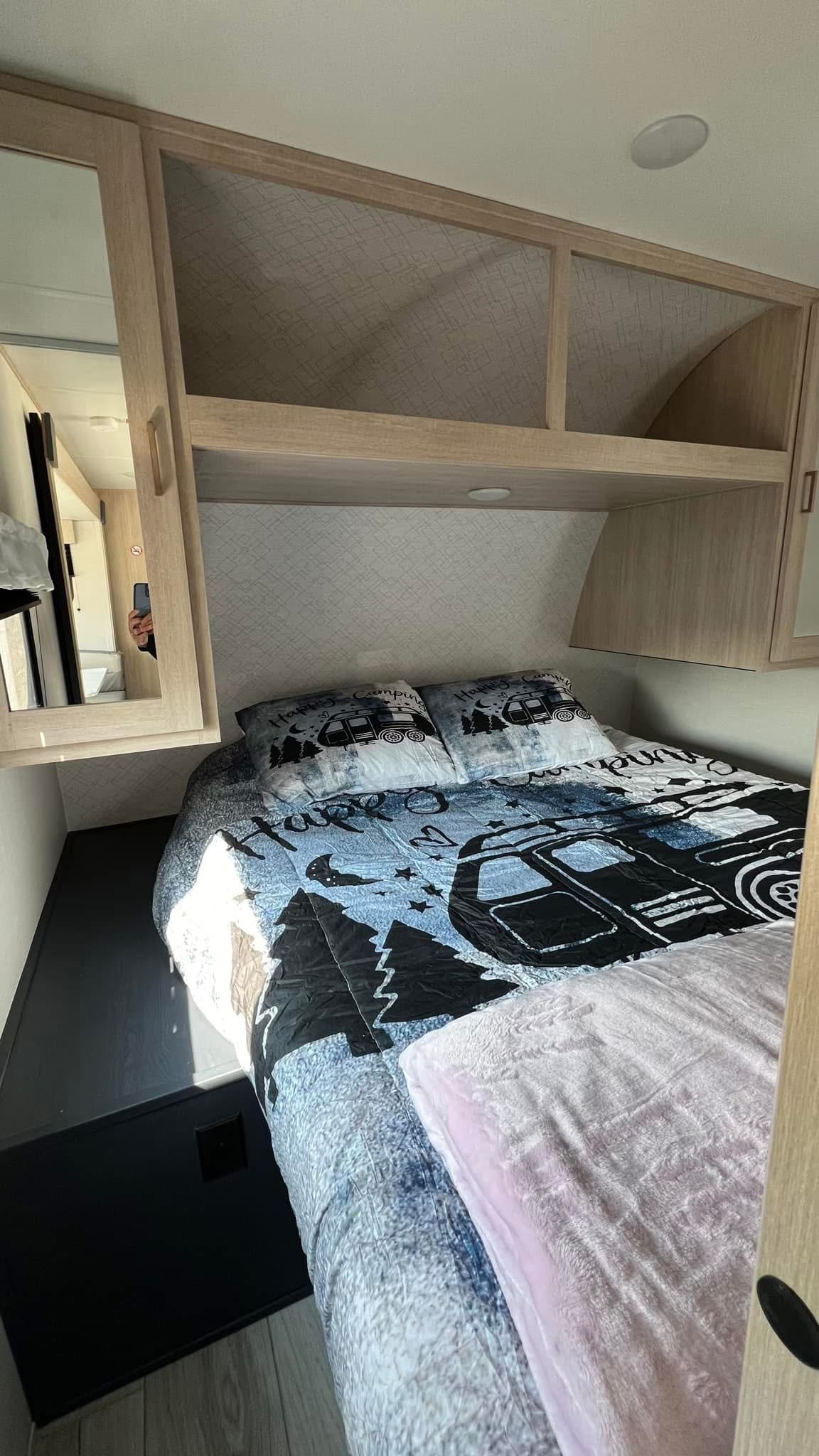 Cozy RV rental bedroom featuring a camping-themed bed, overhead storage, and mirror. Ideal for a comfortable stay.. Prime Time Avenger 2024