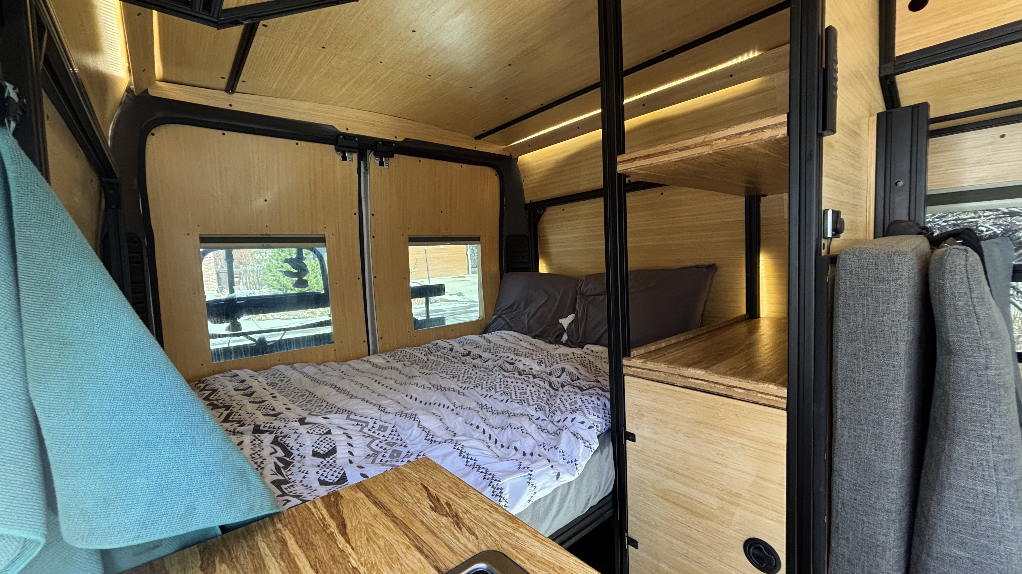 Modern RV rental interior with a cozy bed, wood paneling, and thoughtful storage, bathed in ambient light.. RAM Promaster 1500 2017