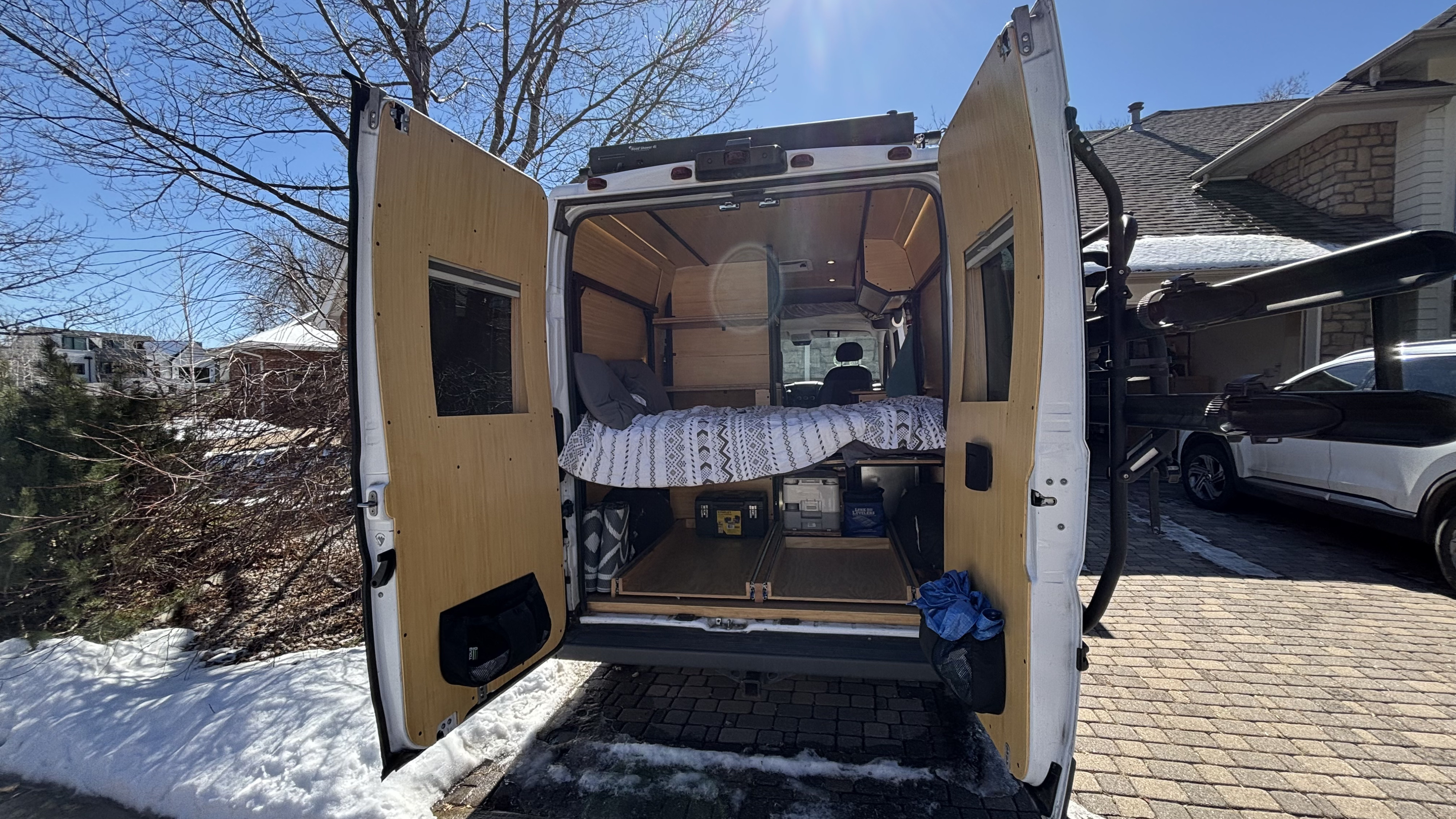 This RV rental camper van shows its cozy bed and storage conversion from the rear, parked on a snowy day.. RAM Promaster 1500 2017