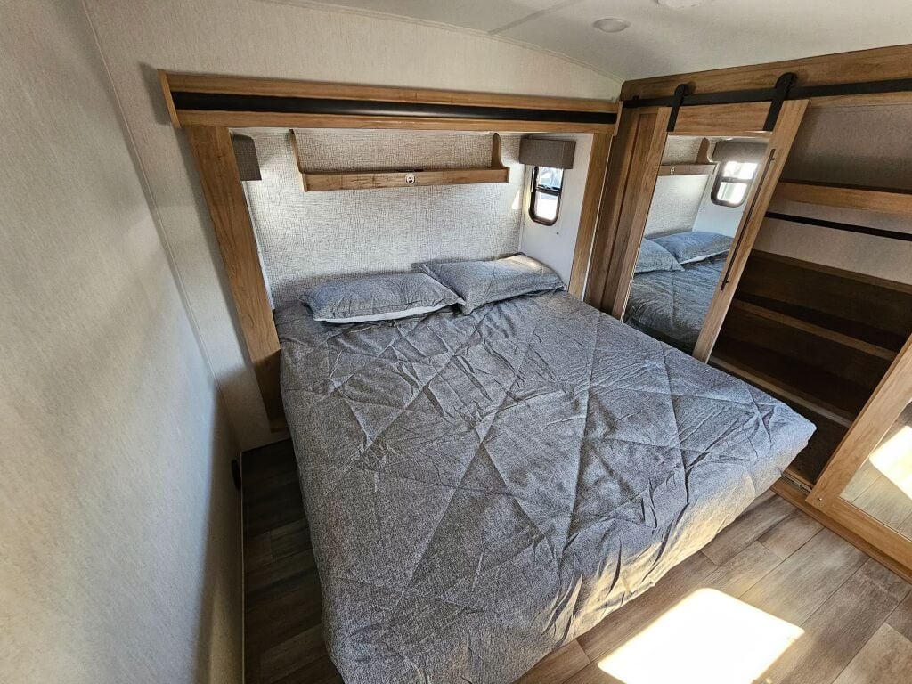 This RV rental's cozy bedroom features a gray bed, built-in shelving, and a mirrored sliding closet. Perfect for travel trailer trips!. Forest River Sabre 38 DBL 2024