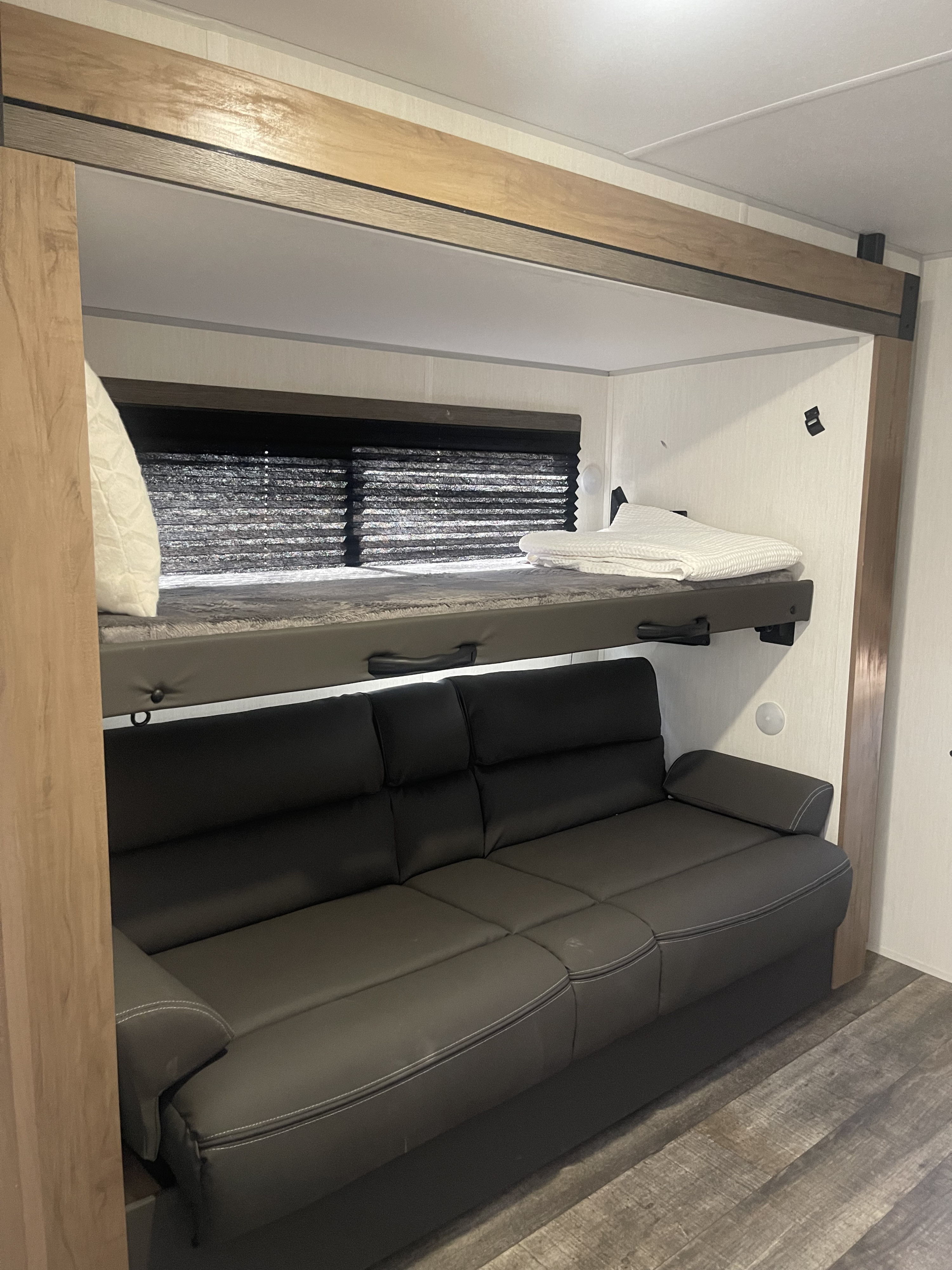 RV rental interior showcasing a cozy light gray bunk bed, complete with bedding, positioned above a dark gray sofa with white stitching.. Forest River Campsite reserve 27MR 2025