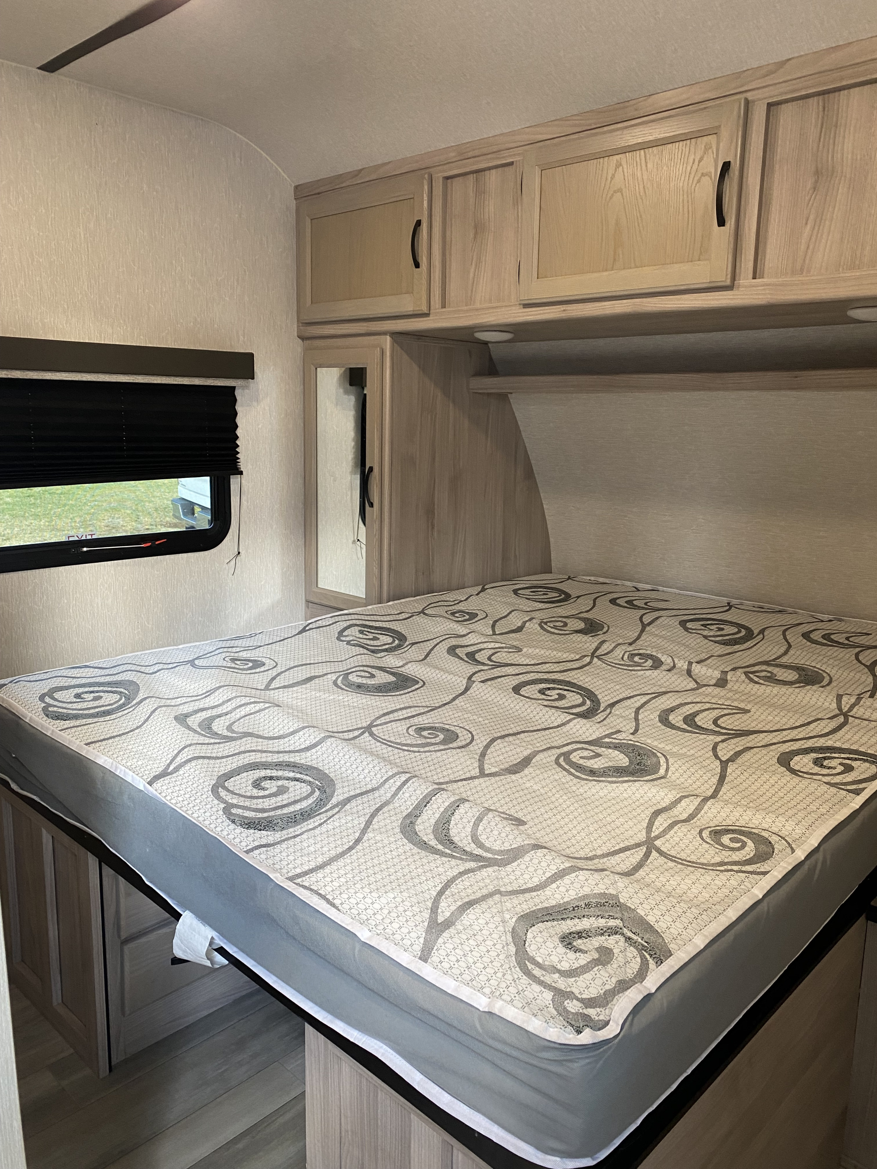 This RV rental bedroom features light wood cabinets, a patterned mattress, and a window with a pulled-down blind.. Coachmen Spirit Ultra light 2021