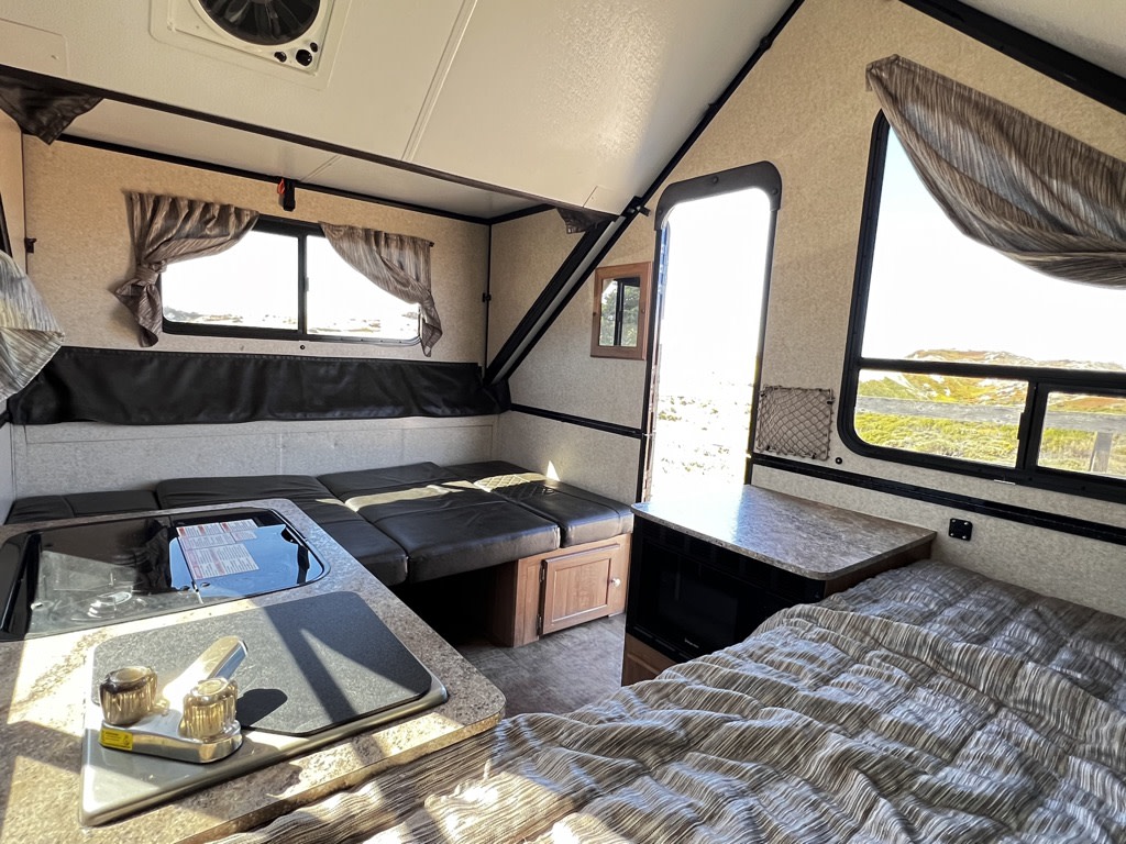Bright RV rental interior: kitchen, flexible seating/bed, and main bed. A compact, complete living space for adventure.. Forest River A122BH 2018
