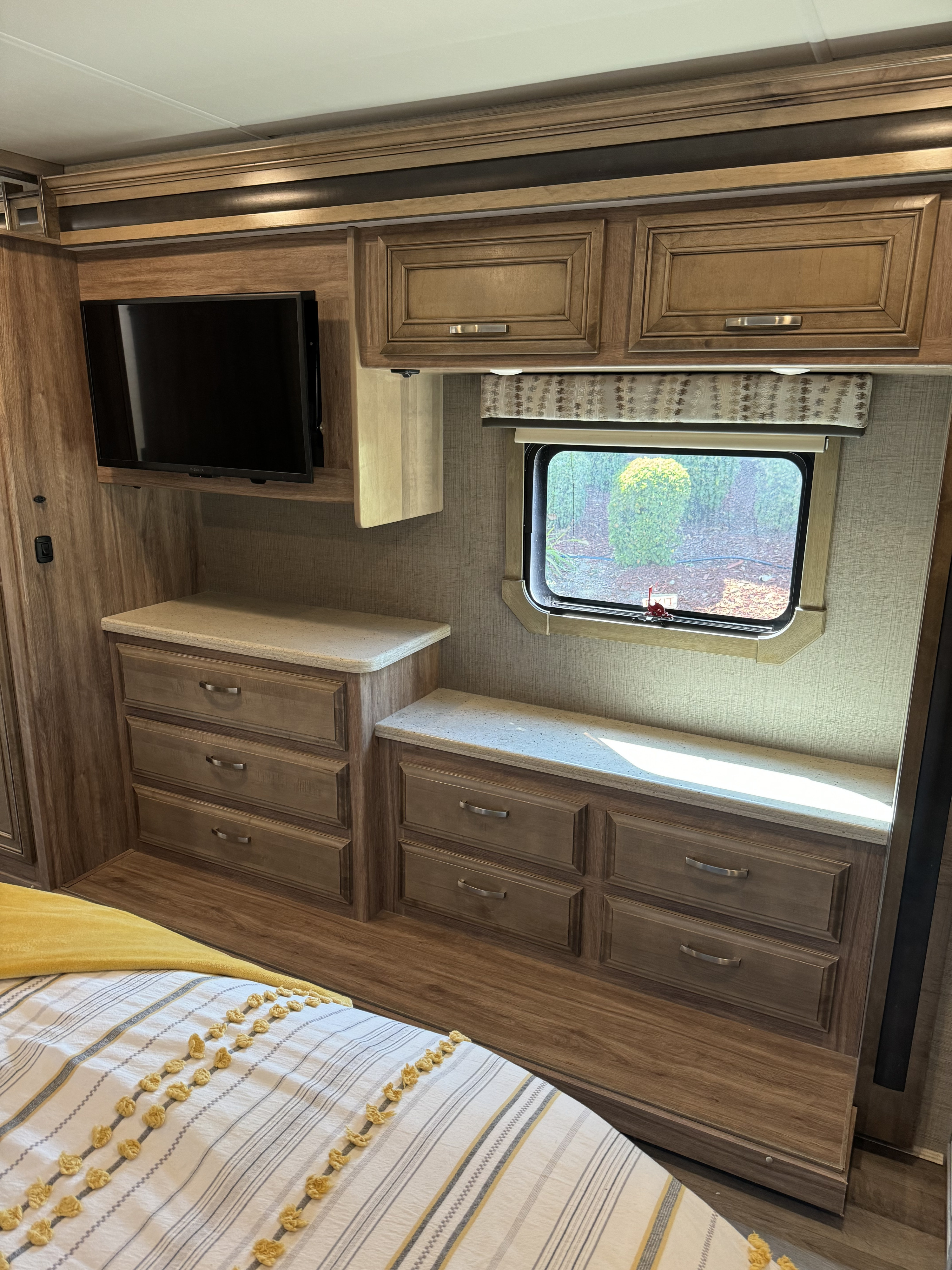 RV rental bedroom: TV, overhead and drawer storage, window with outdoor view, and striped bedspread.. Jayco Precept Prestige 2021